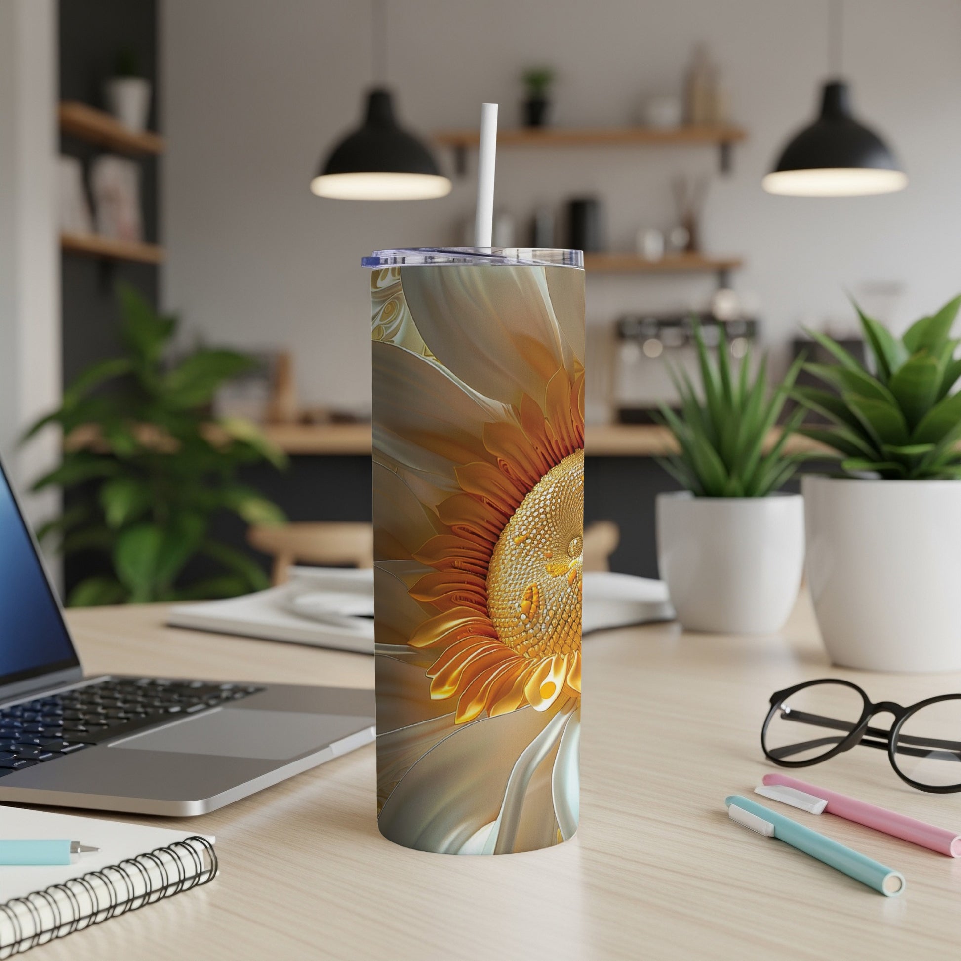Sunflower tumbler with straw on desk with laptop and pens.