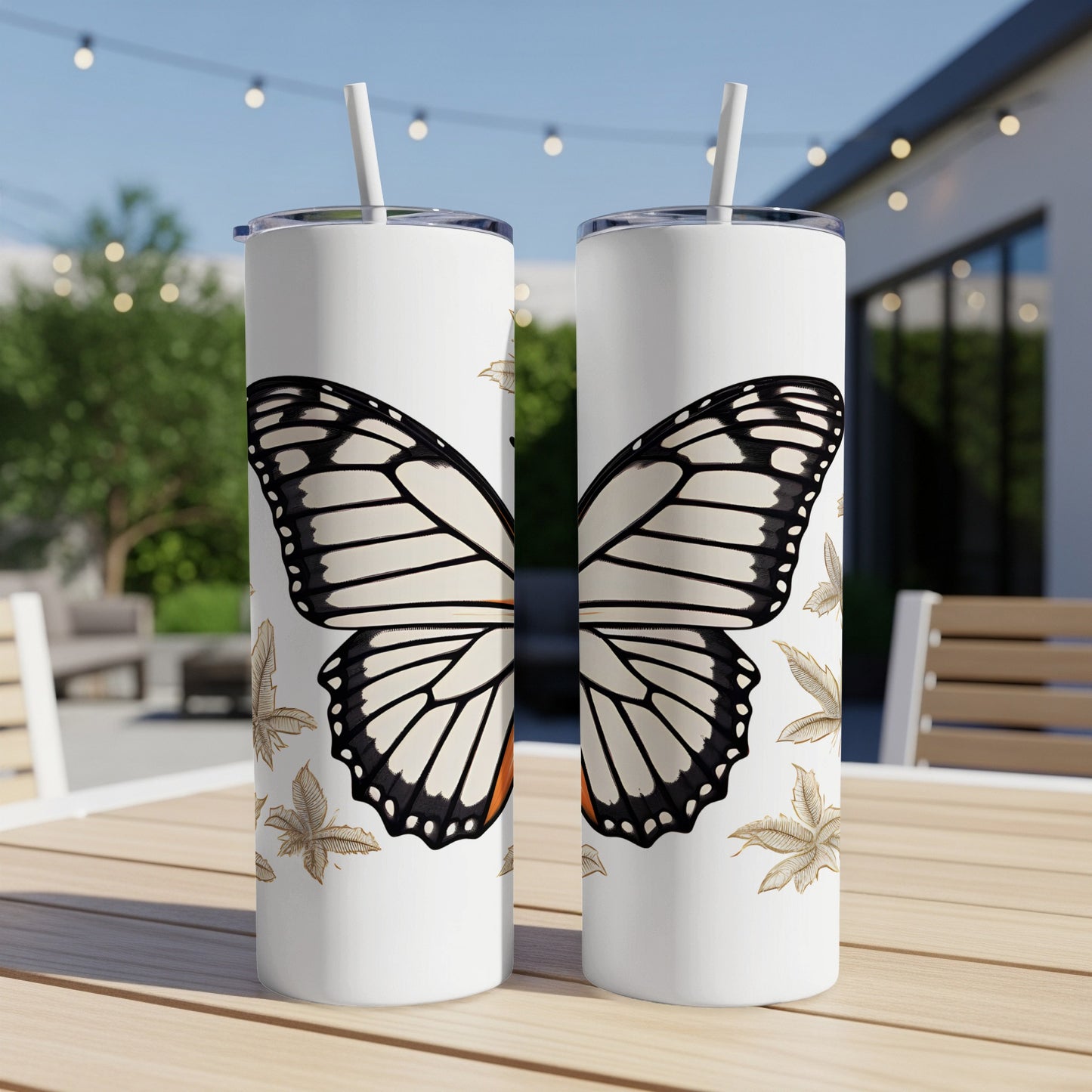 Two white tumblers with monarch butterfly design sit on a patio table.