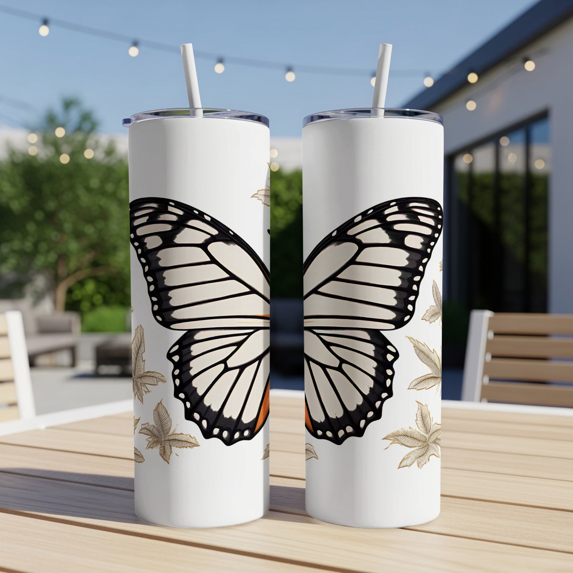 Two white tumblers with monarch butterfly design sit on a patio table.