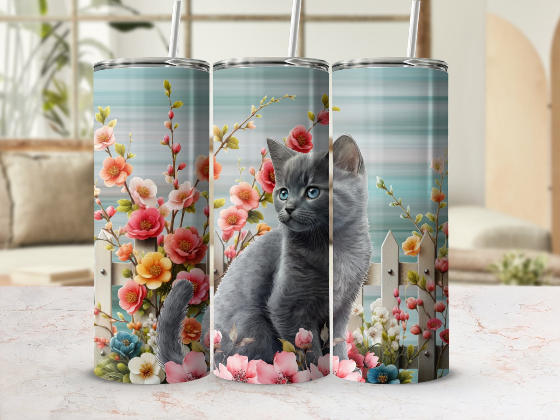 Gray kitten with blue eyes sits behind a white picket fence with floral accents.