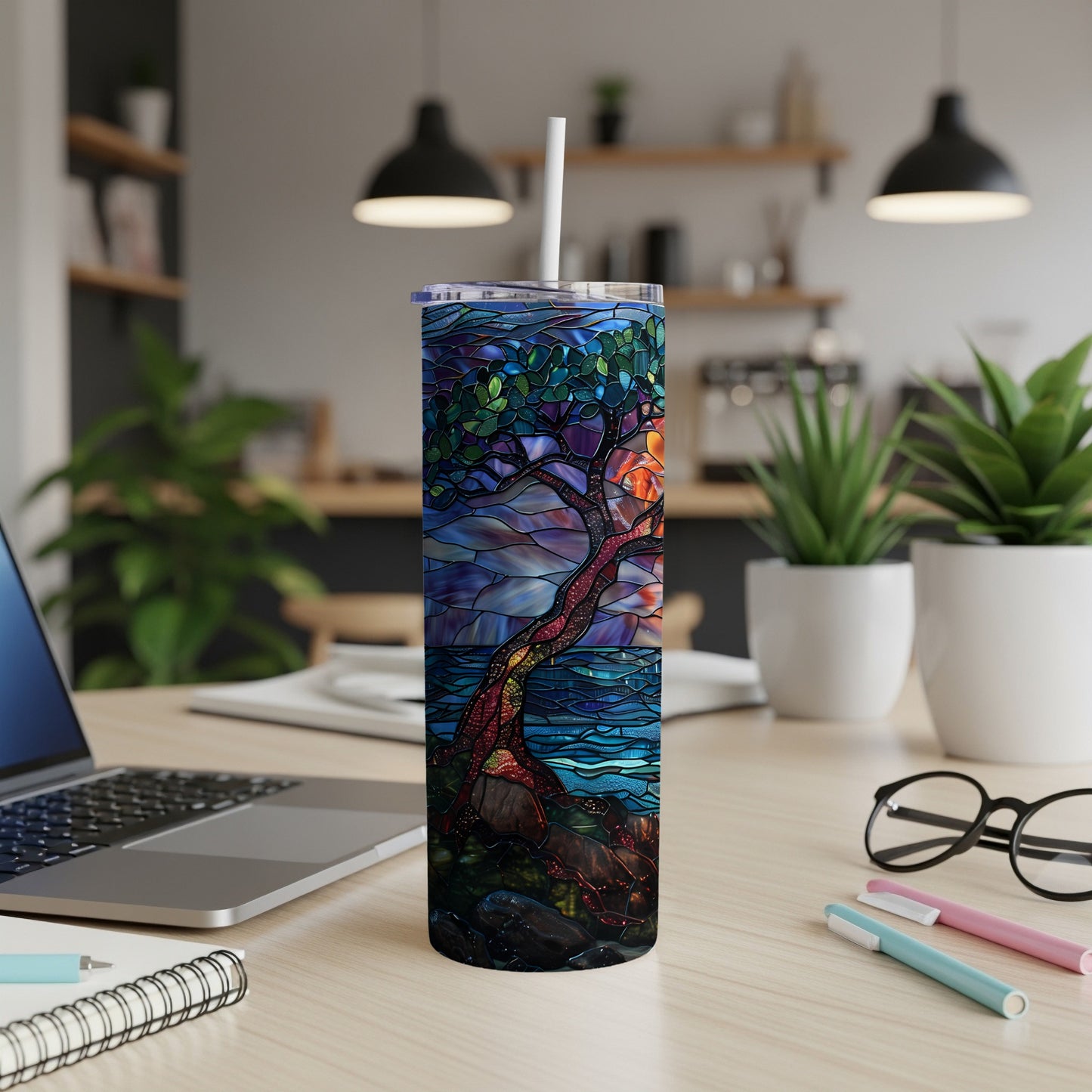 Tall tumbler with stained glass tree design on wooden desk with laptop.