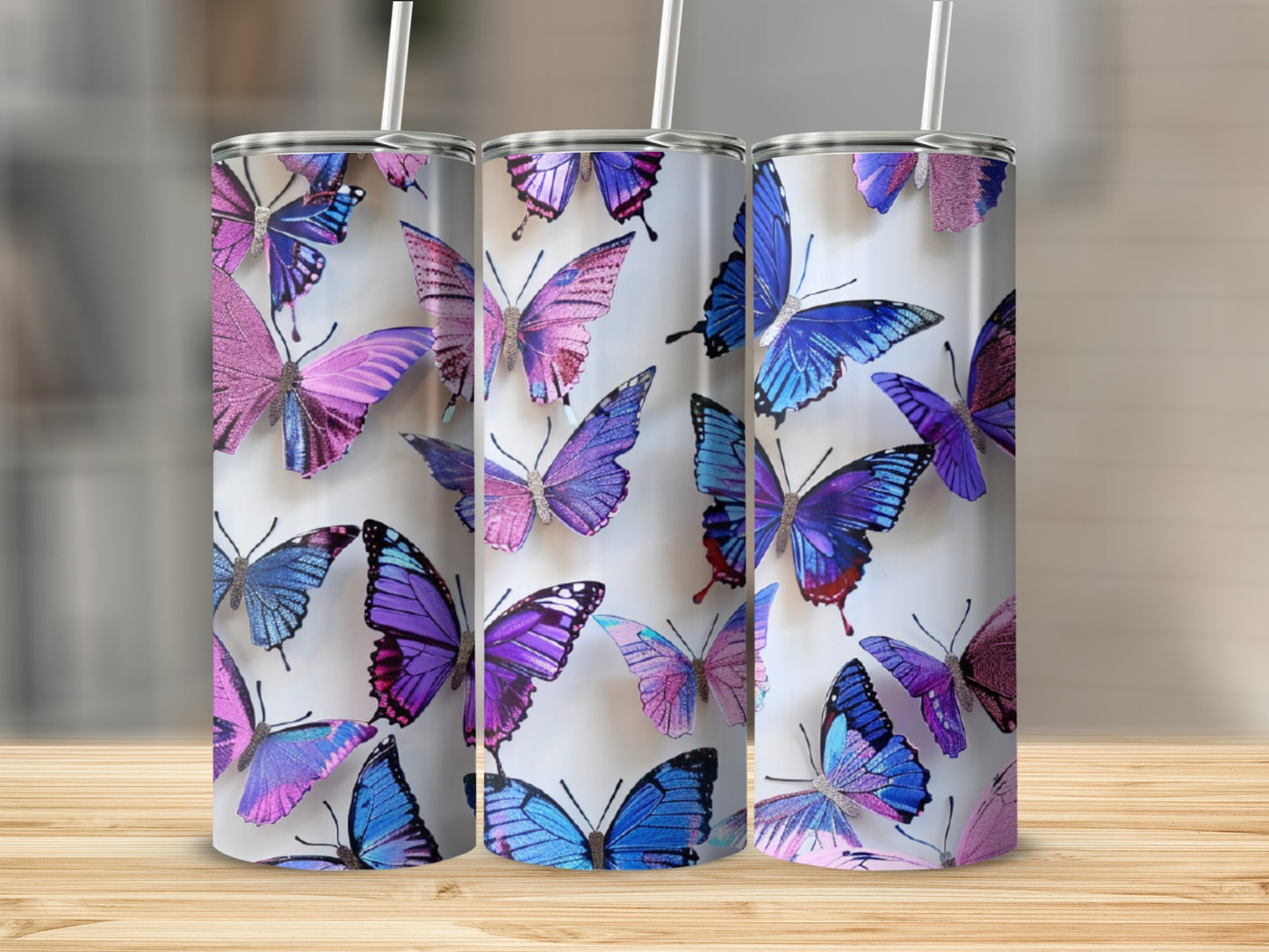 Three tumblers with colorful butterfly designs on a wooden surface.
