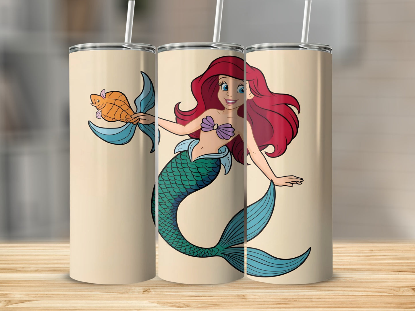The Little Mermaid holding a gold fish with straw, displayed on a wooden surface.