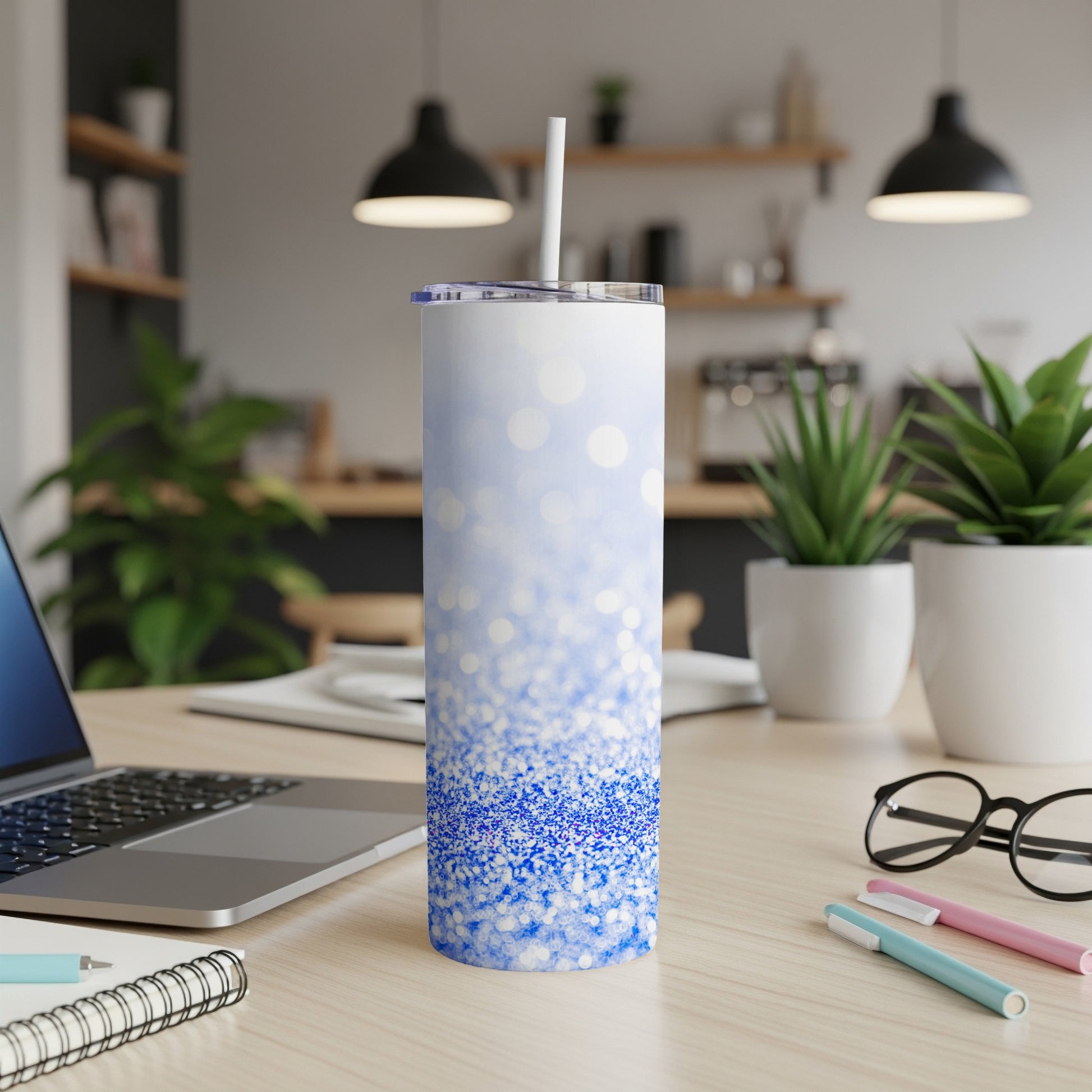 White and blue glitter tumbler with straw on a desk.