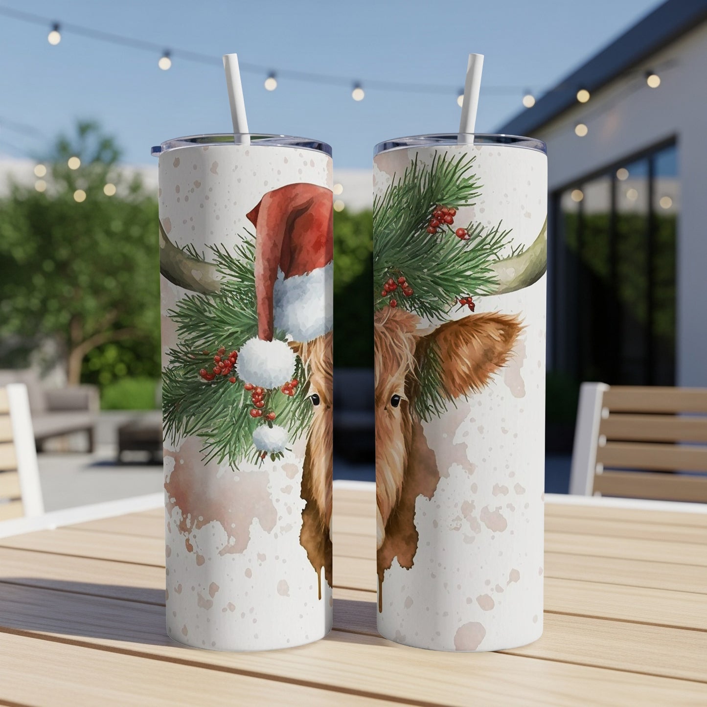 Two highland cows wearing Santa hats and pine garland on tumblers.