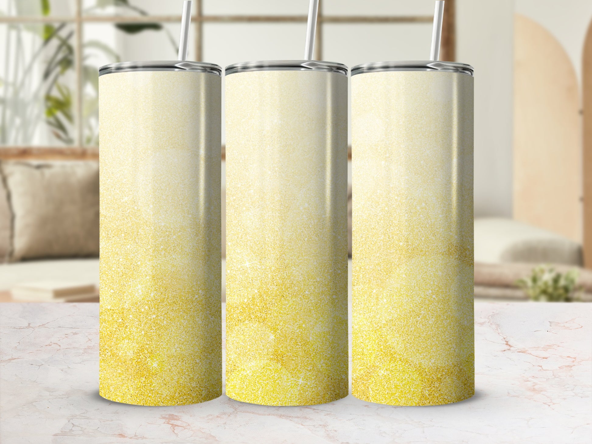 Three glittery gold tumblers with straws on a marble surface.