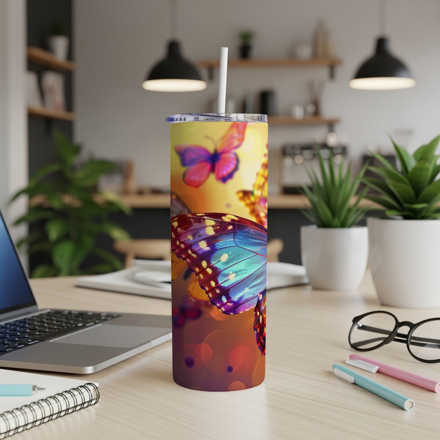 Colorful butterfly tumbler with straw on a desk with a laptop and pens.