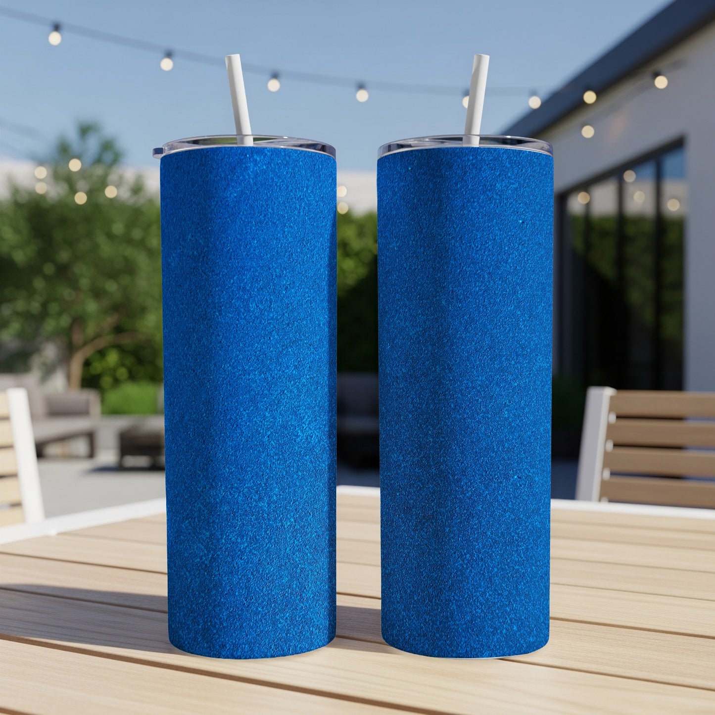 Two blue glitter tumblers with straws on a wooden table.