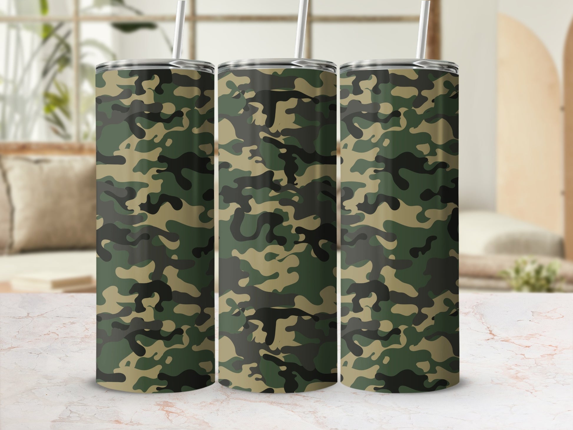 Three tumblers with camouflage pattern and metal straws on a marble surface.