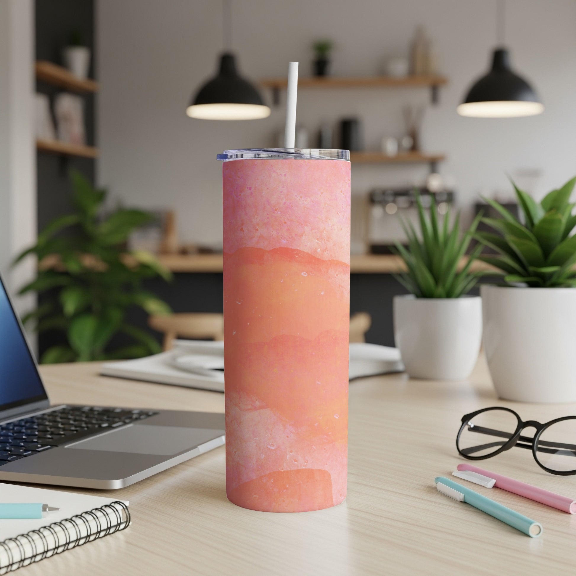 Pink and orange marbled tumbler with straw on a desk.