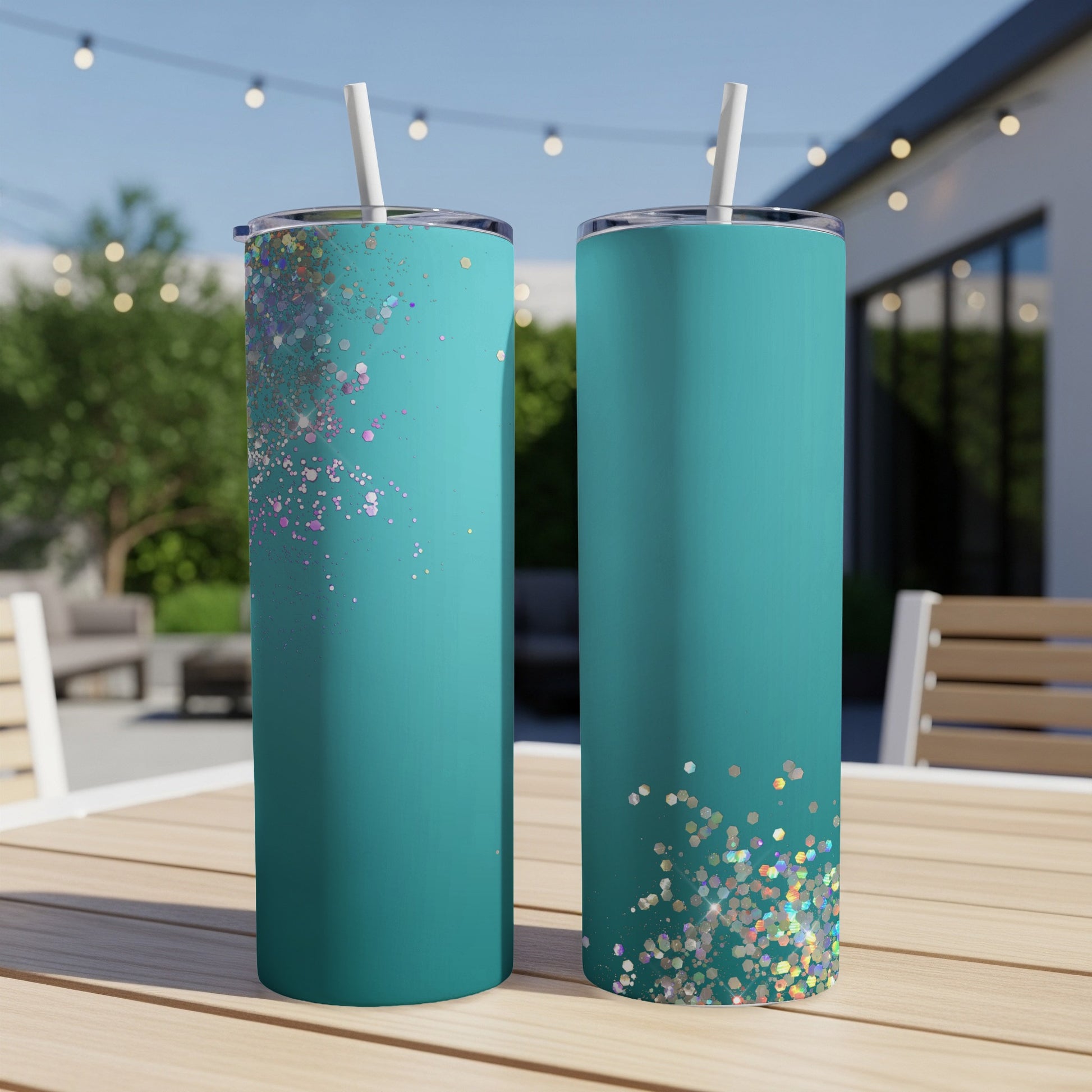 Two teal tumblers with glitter accents displayed on a wooden table outdoors.