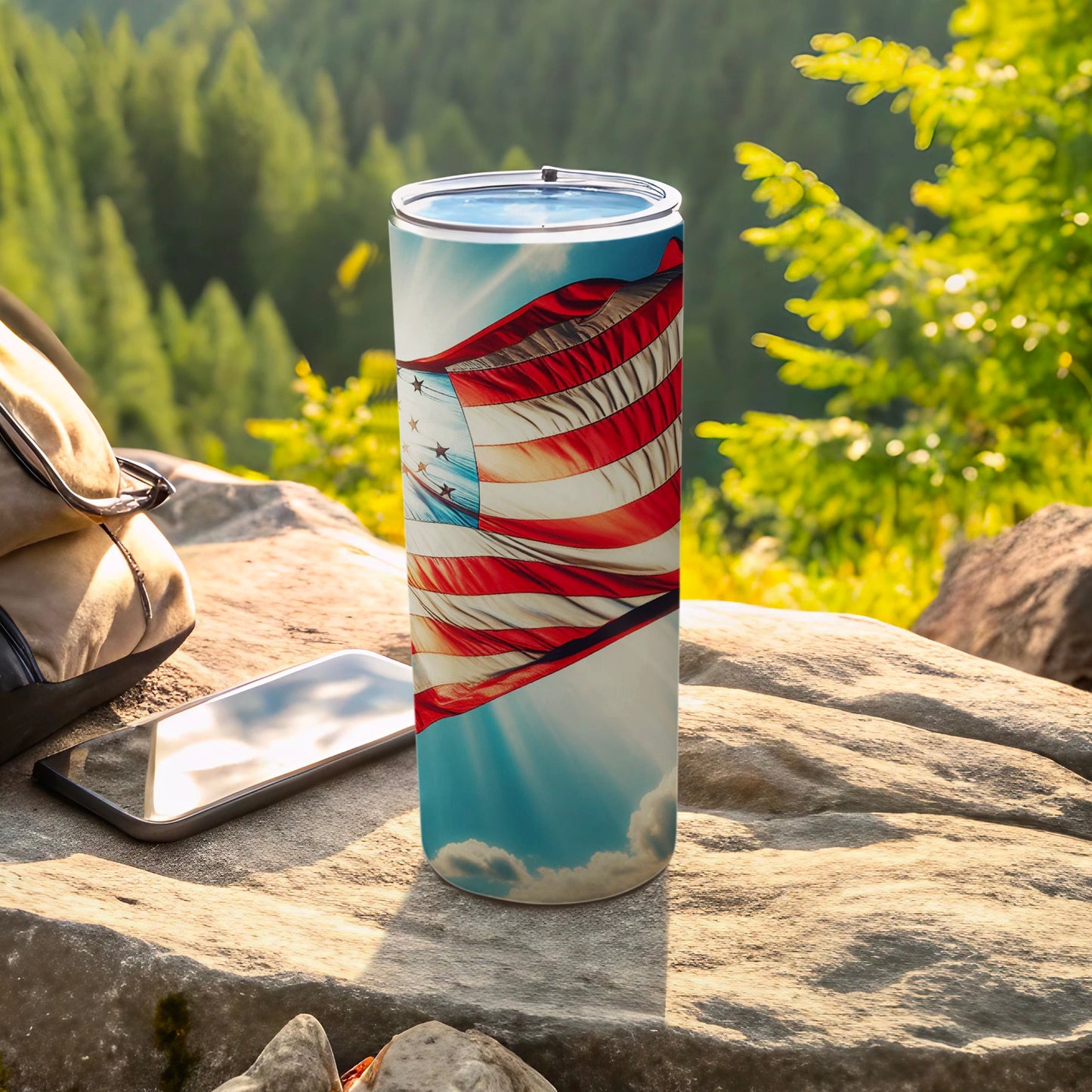 American flag tumbler on rocky surface with backpack and phone.