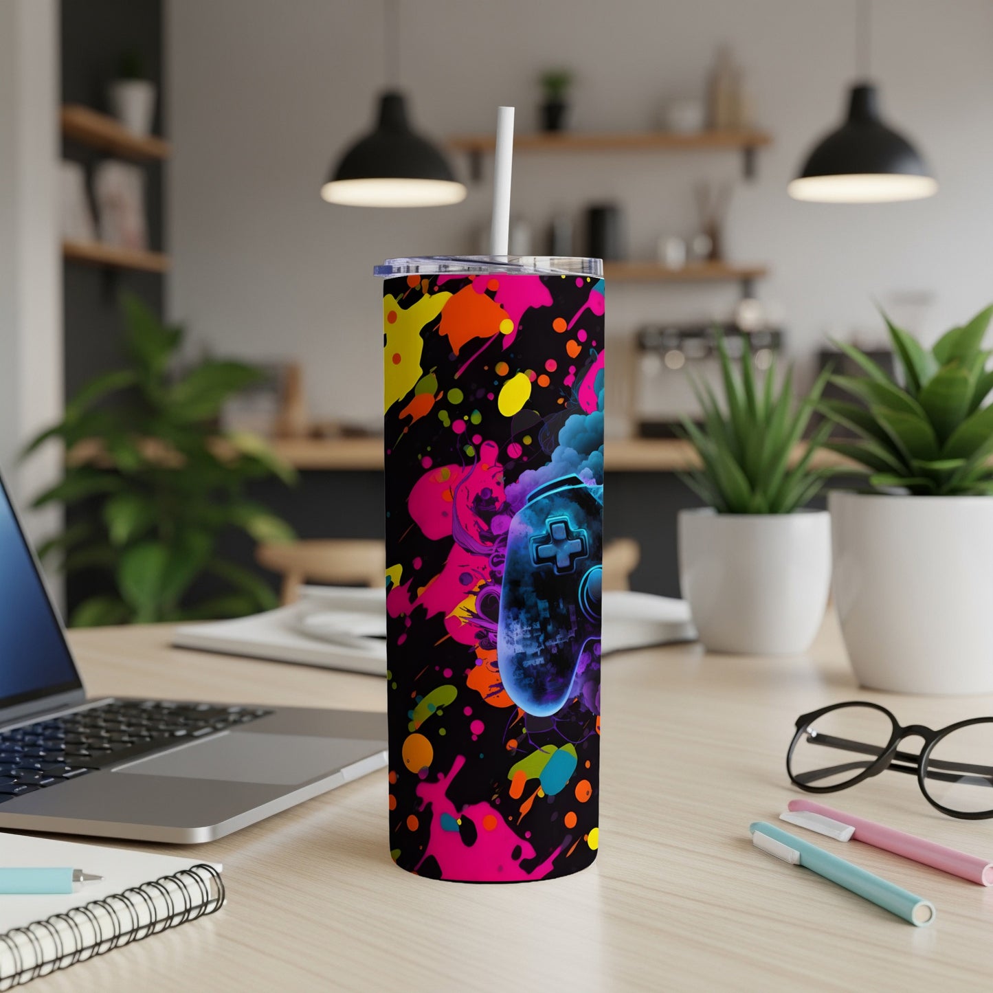 Gaming controller tumbler with neon paint splatter design on a desk.