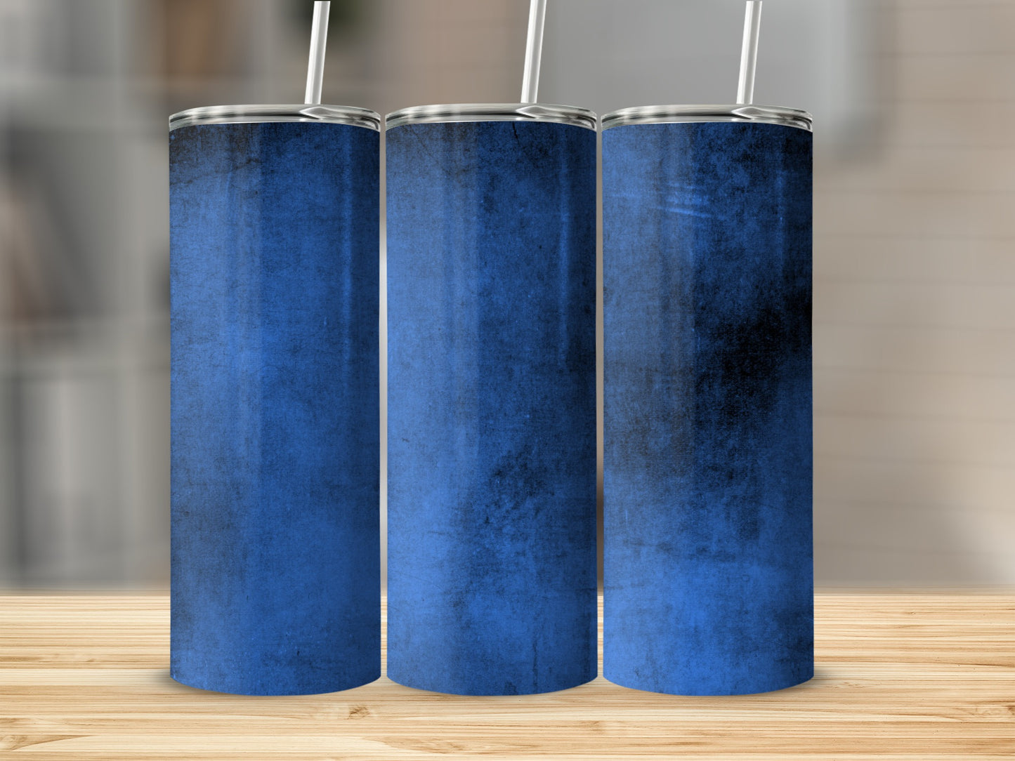 Three blue tumblers with textured grunge design and straws on wooden surface.