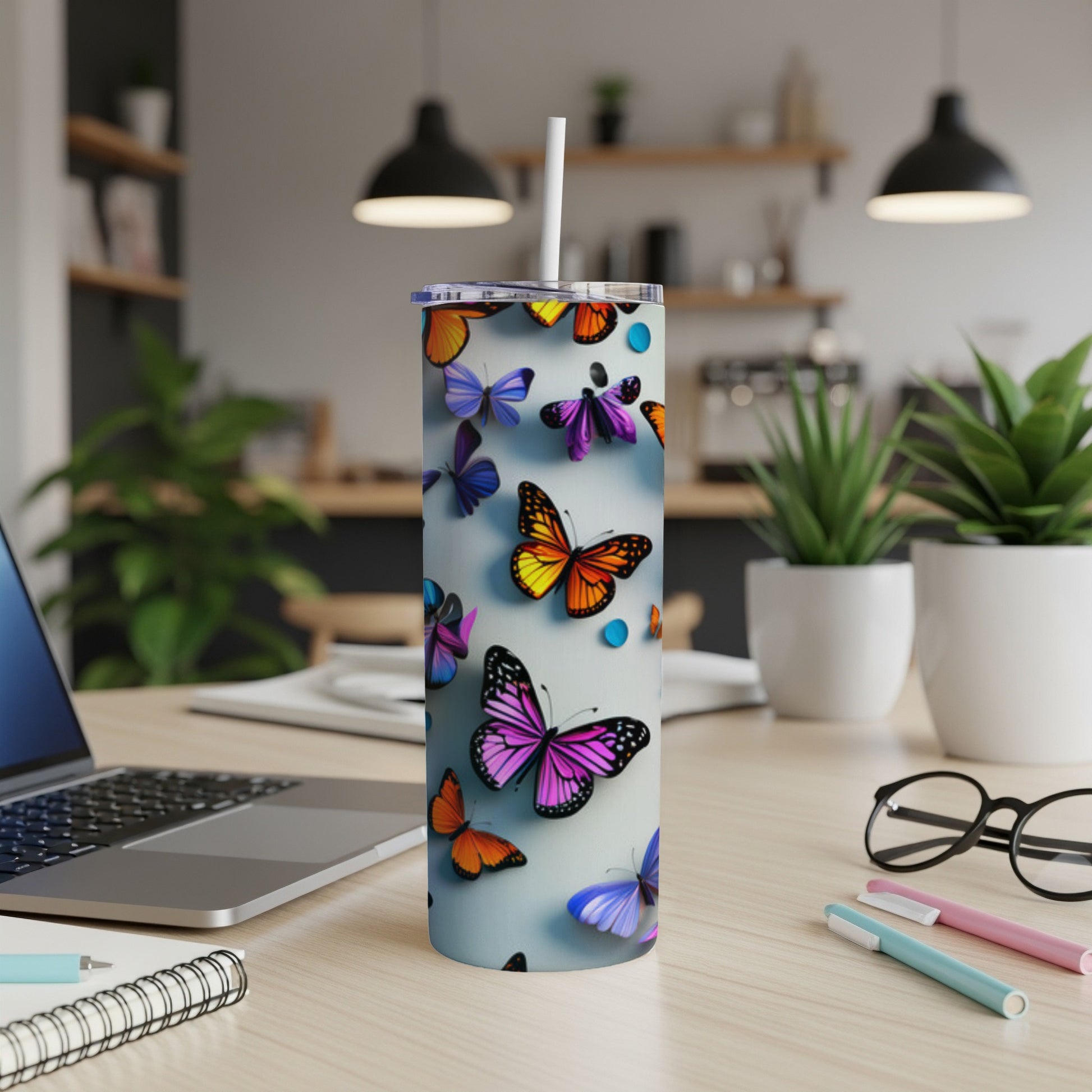 Tall tumbler with colorful butterflies, on a desk with a laptop and pens.