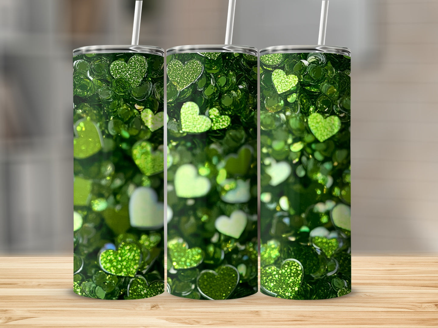 Three green glitter heart tumblers with straws on a wooden surface.