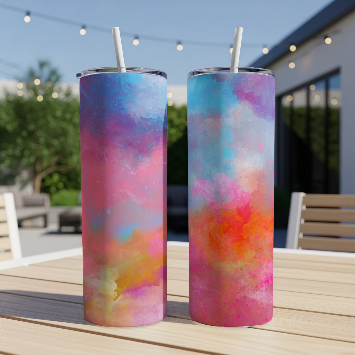 Two tumblers with colorful watercolor splashes and white straws on a wooden table.