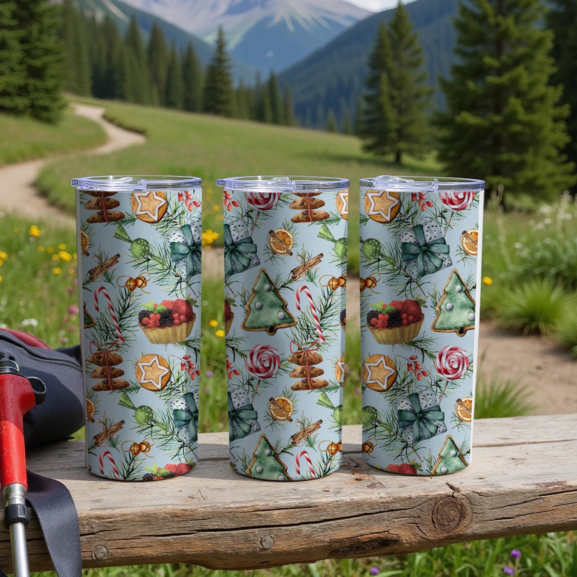 Three tumblers with Christmas patterns sit on a wooden table outdoors.
