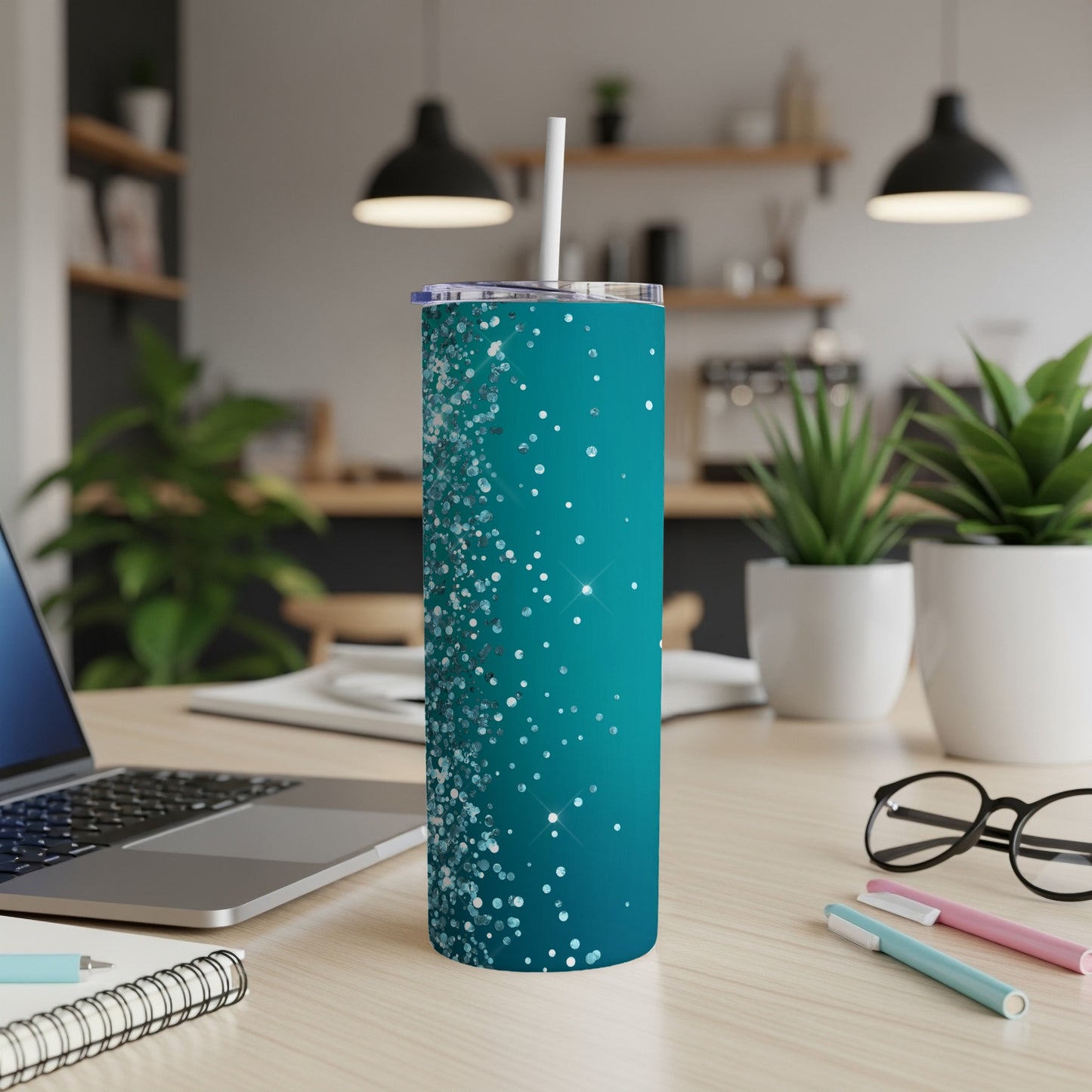 Teal tumbler with glitter and sparkle design and straw, on a desk.