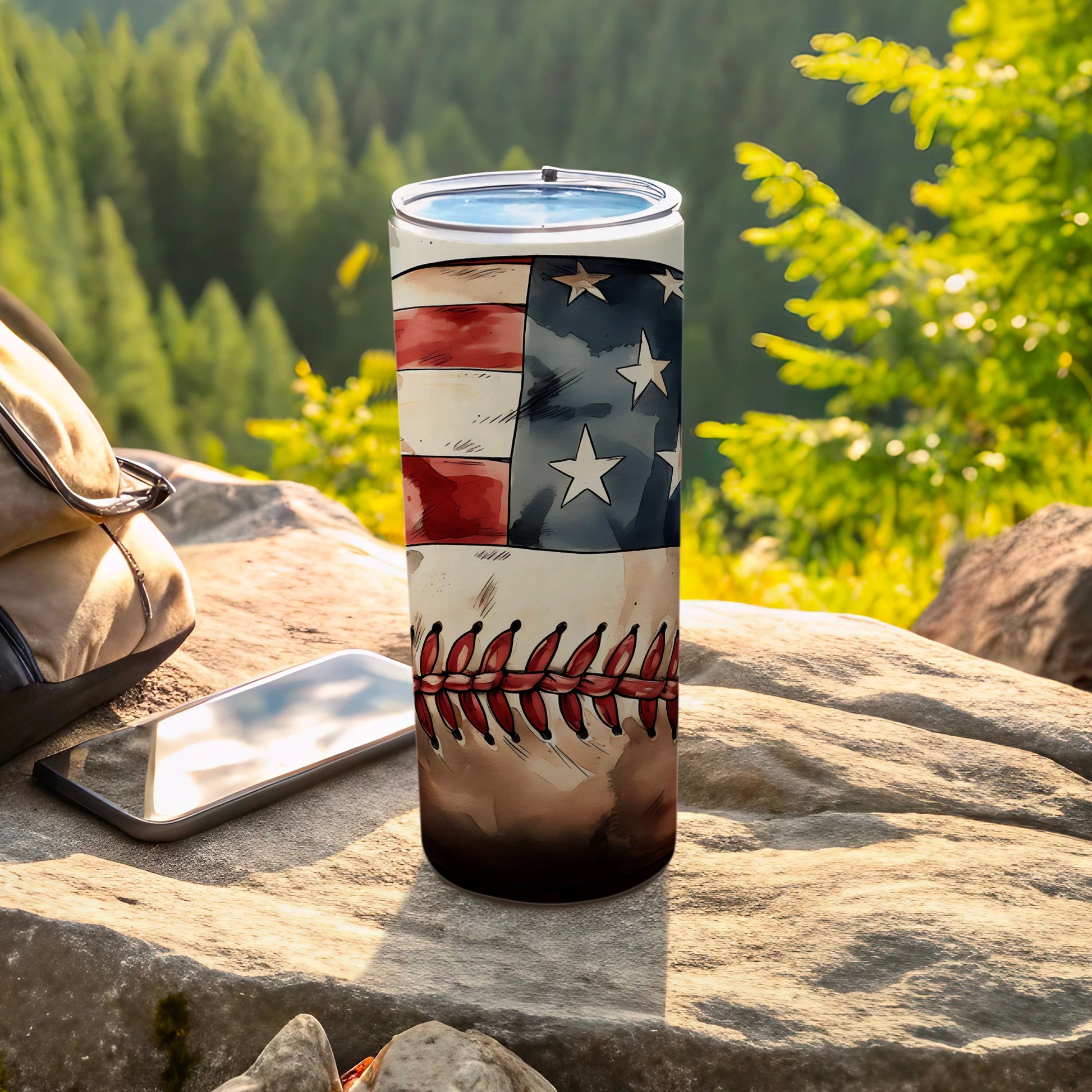 Tumbler with American flag and baseball stitching design on rocky surface.