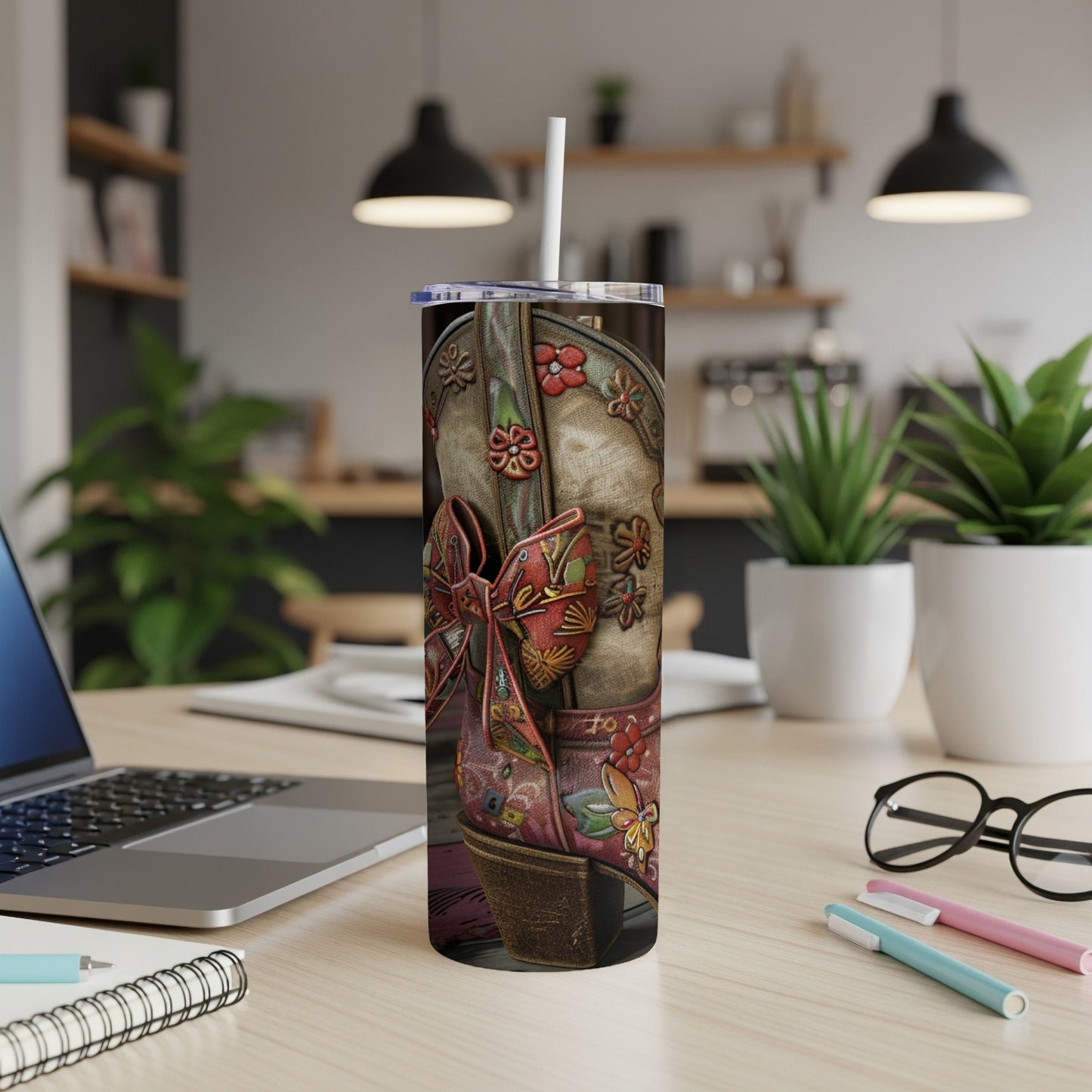 Cowboy boot tumbler with floral accents and red bow on a desk.