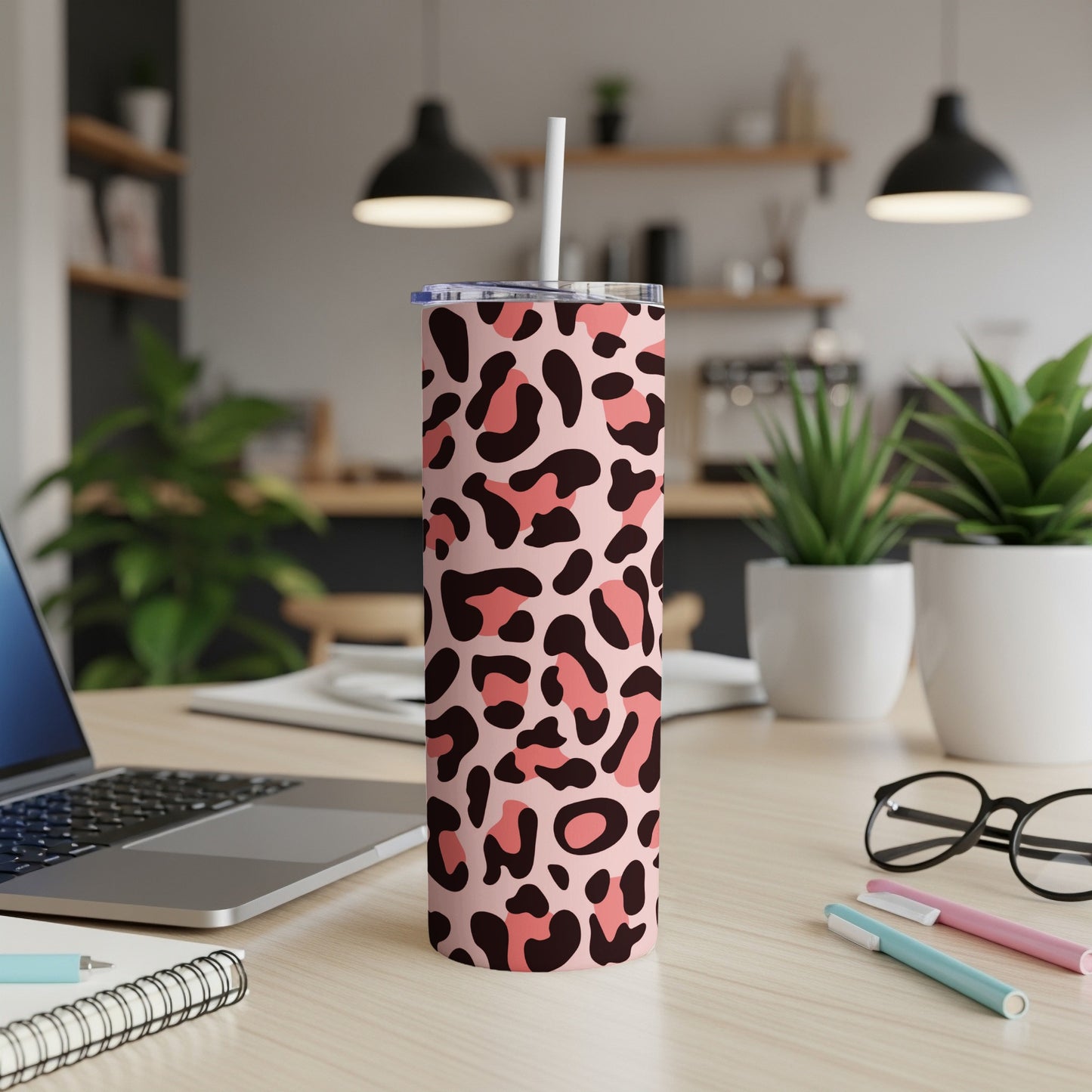 Pink leopard print tumbler with straw on a desk with laptop and plants.