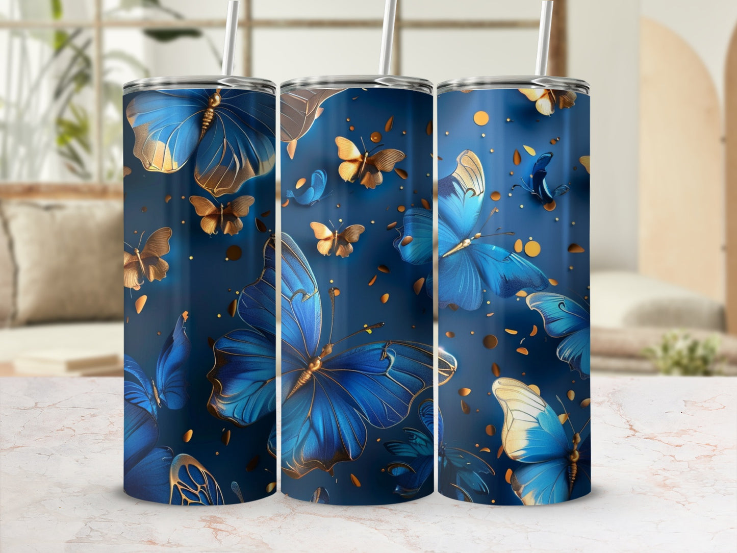 Three blue and gold butterfly tumblers with straws on a marble surface.