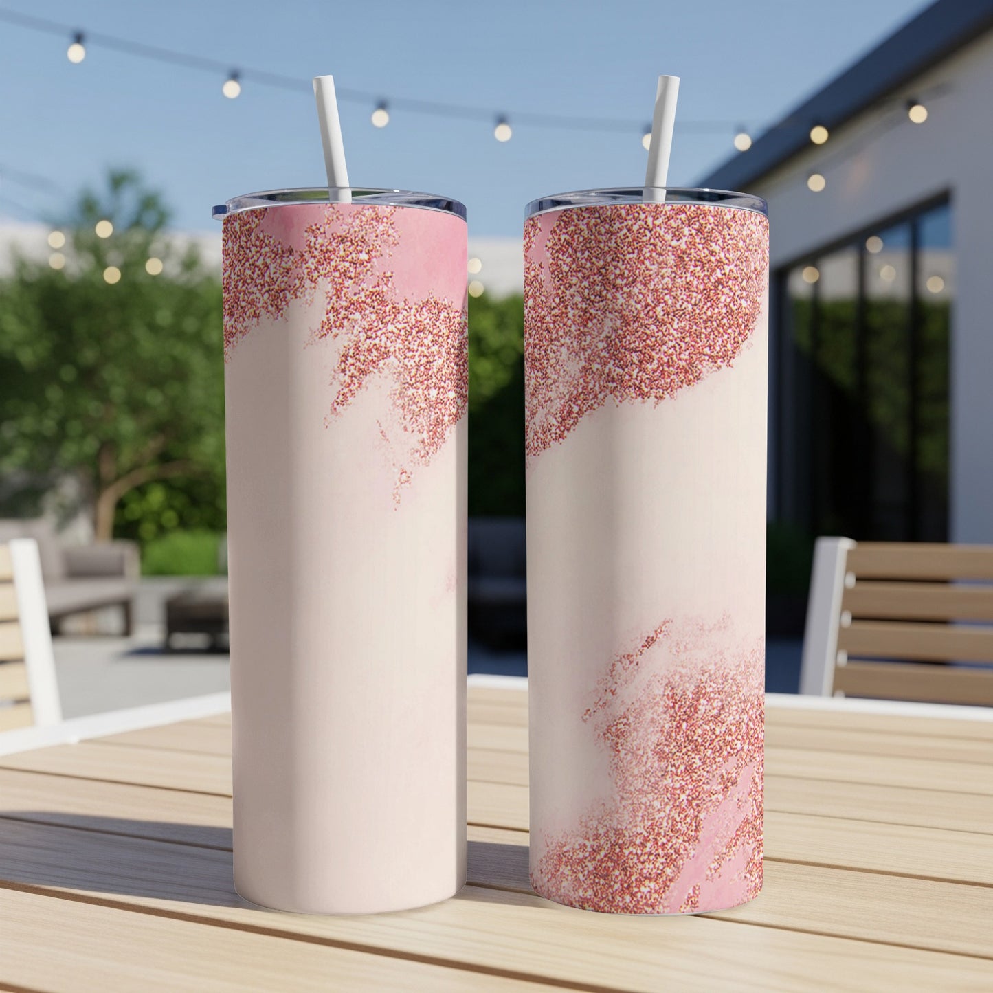 Two pink glitter tumblers with straws on a table outdoors.