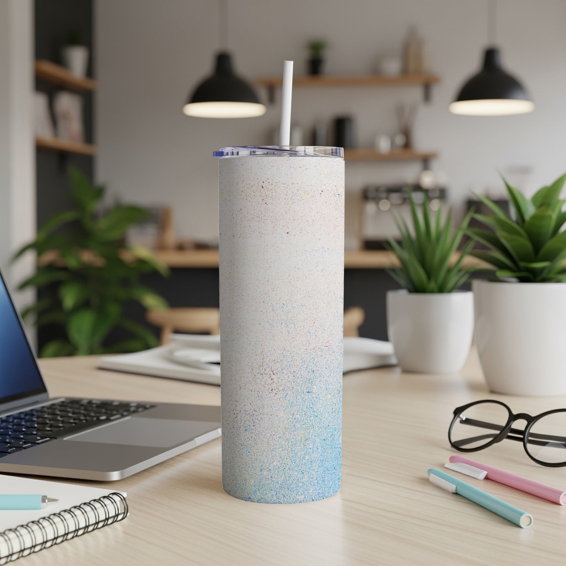 White speckled tumbler with straw on a desk next to a laptop.