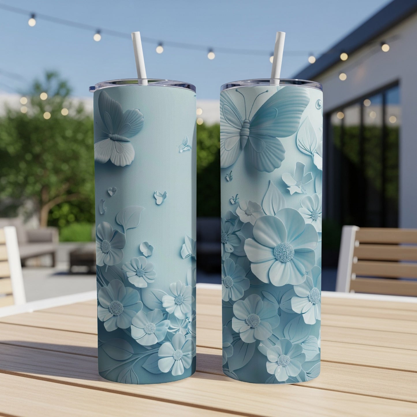 Two blue tumblers with embossed floral and butterfly designs on a wooden table.