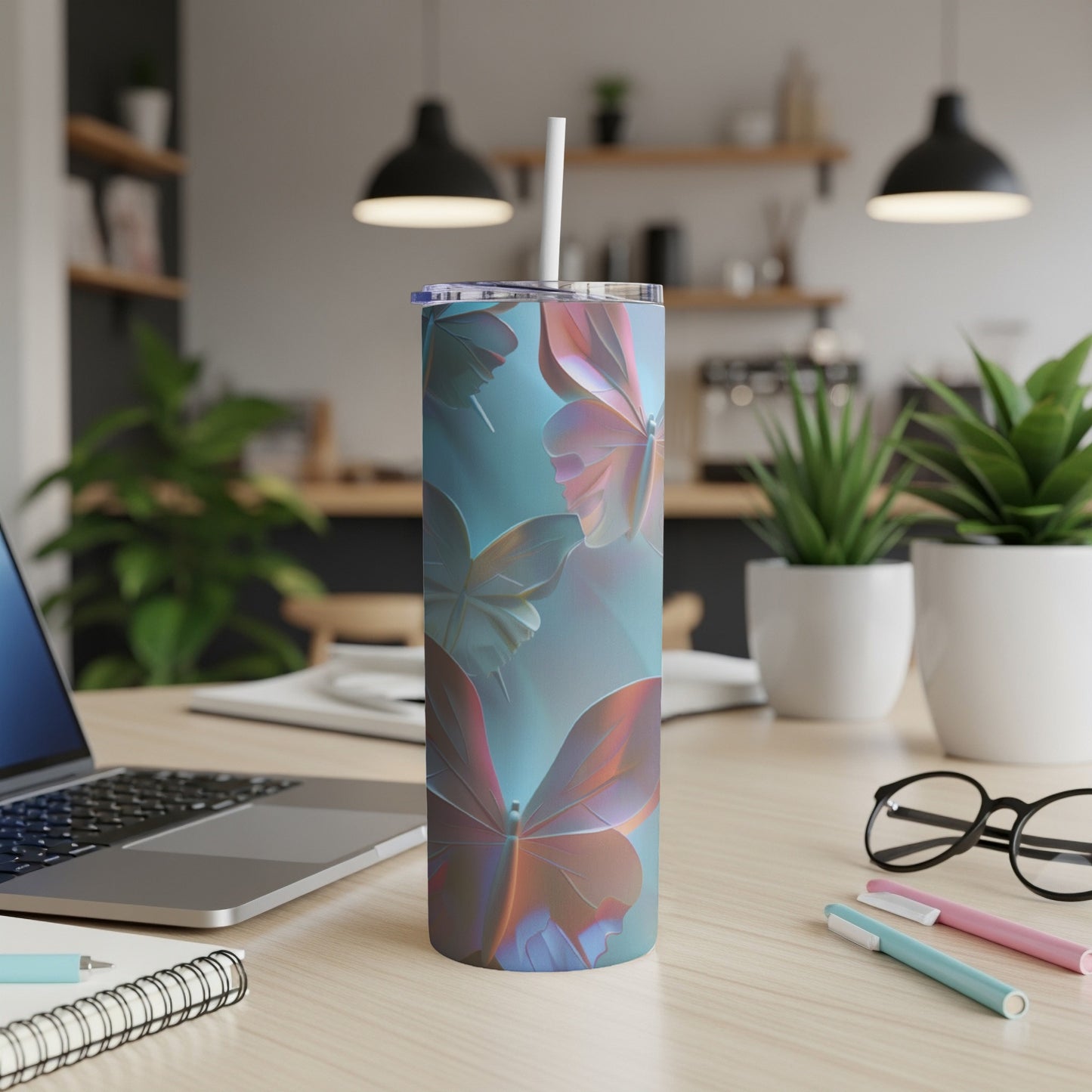 Tall tumbler with colorful butterfly design on desk with laptop and pens.