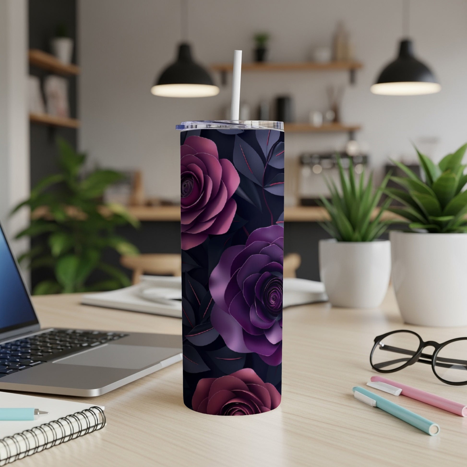 Purple floral tumbler with straw on a desk with a laptop and pens.