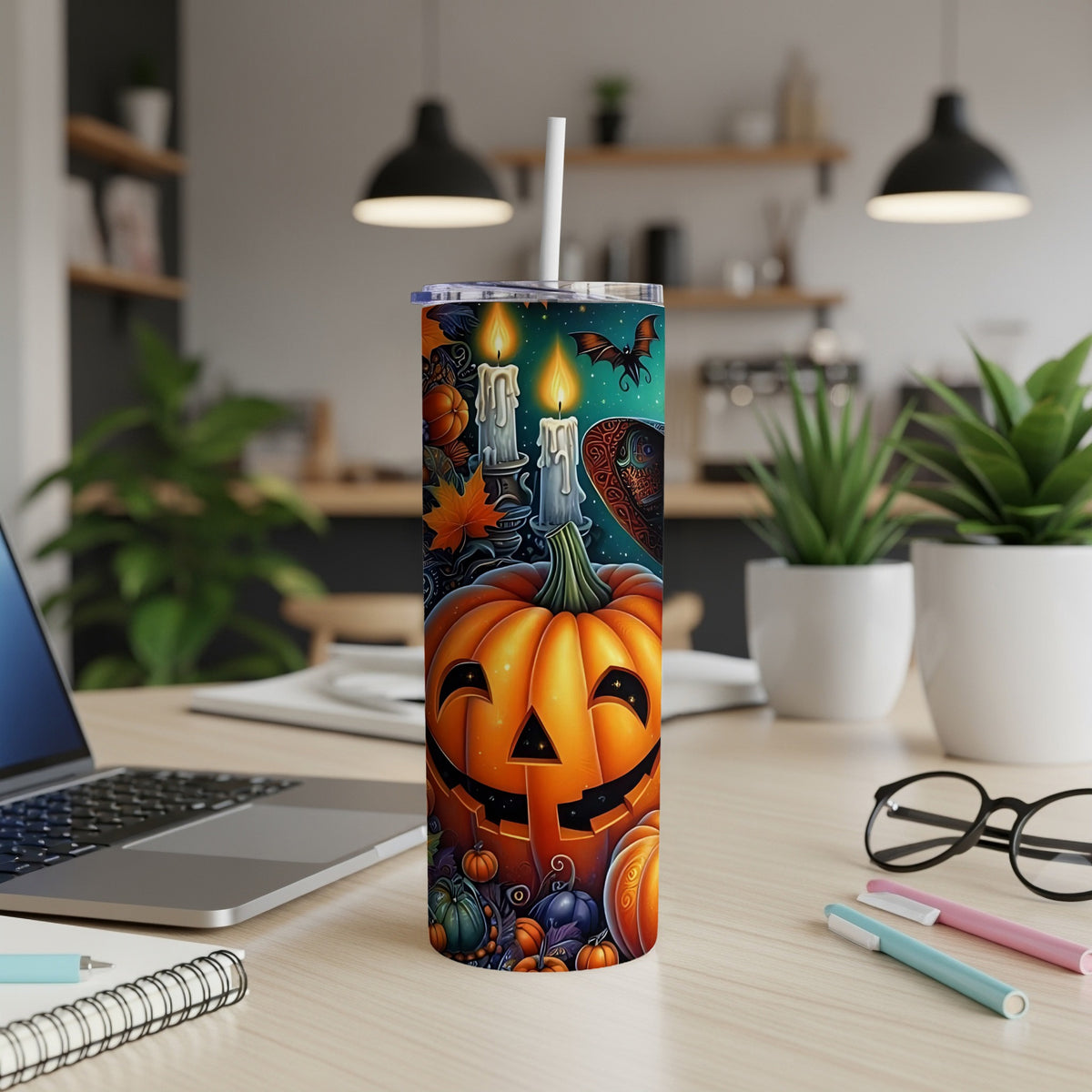 Halloween tumbler with pumpkins, bats, and candles on a desk with a laptop.
