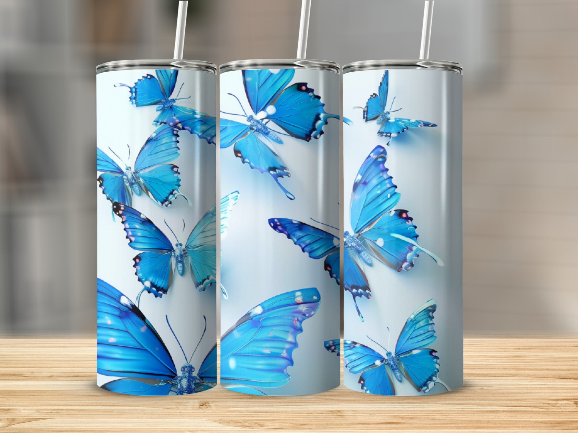Three tumblers decorated with bright blue butterflies on a wooden surface.