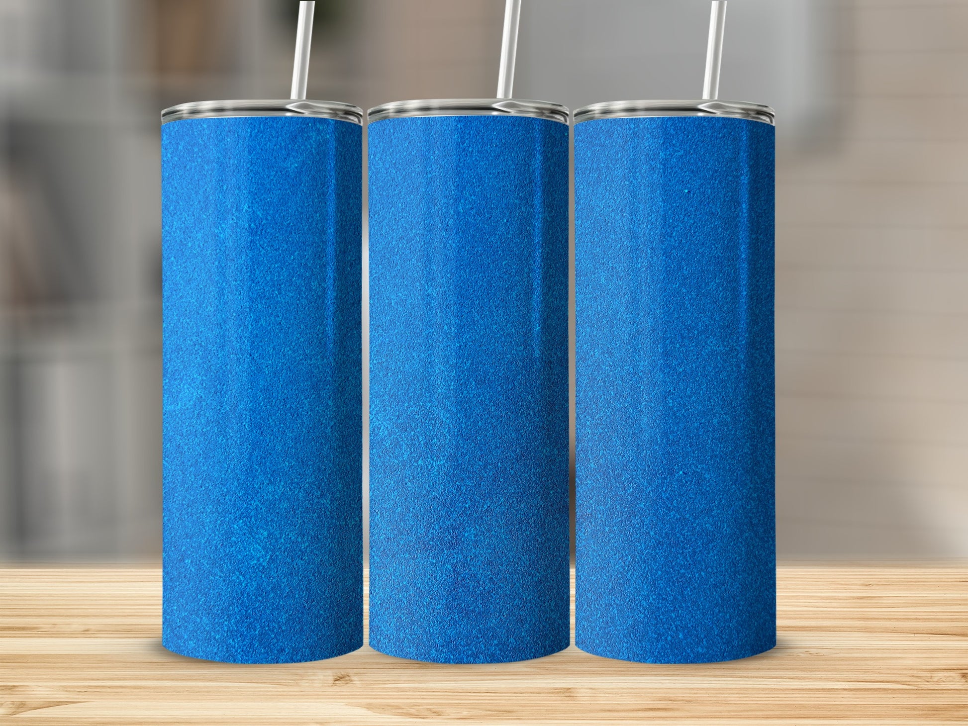 Three tall, glittery blue tumblers with white straws on a wooden surface.