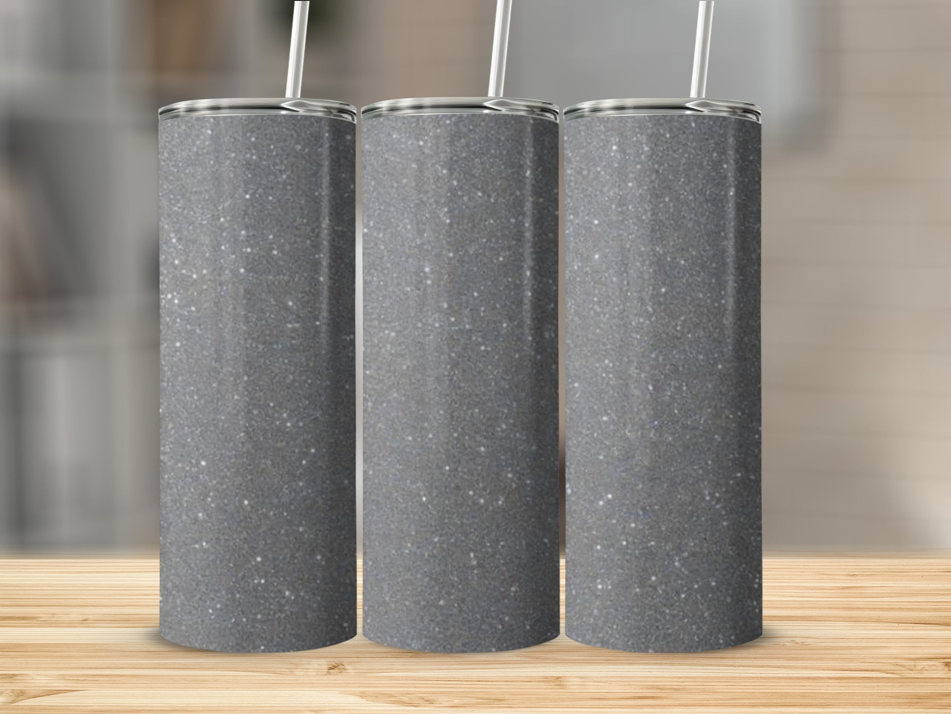 Three glittery grey tumblers with white straws on a wooden surface.