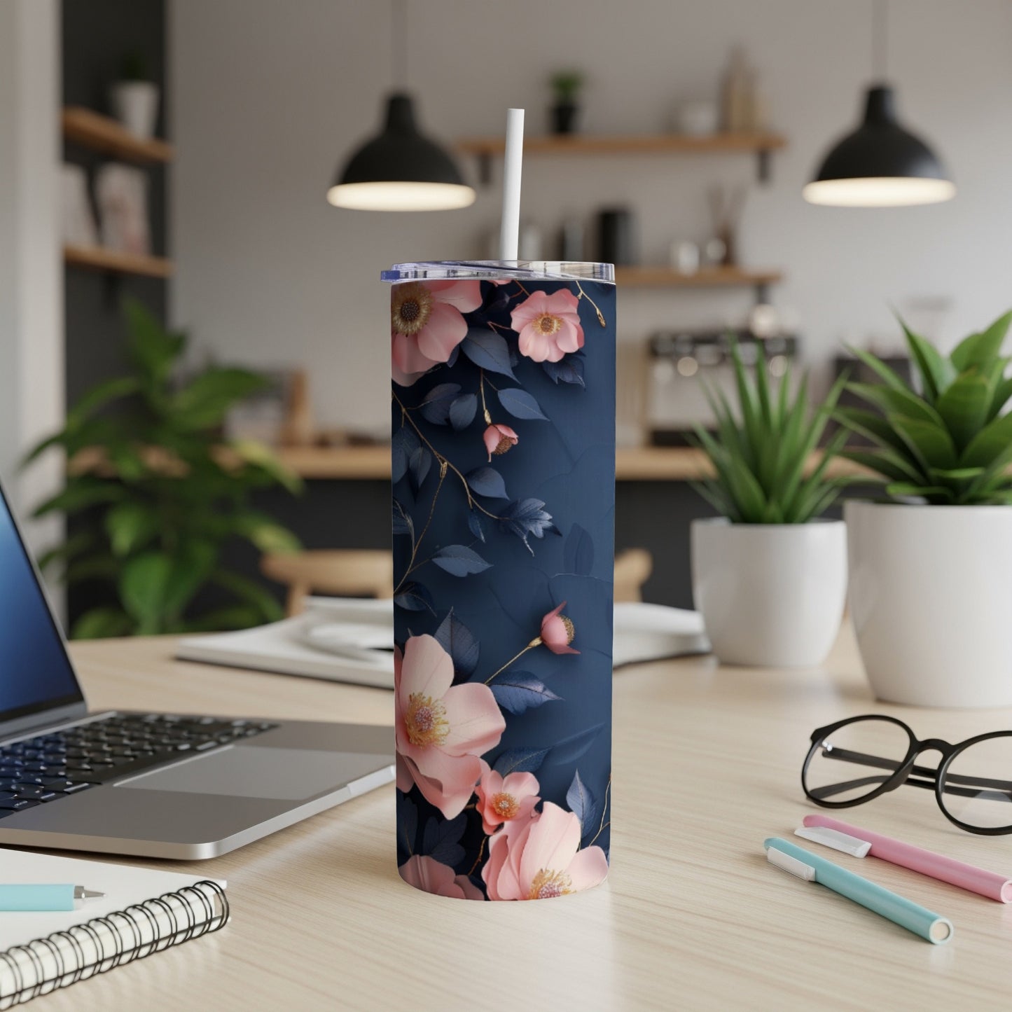 Dark blue tumbler with pink floral pattern, straw, on a desk.