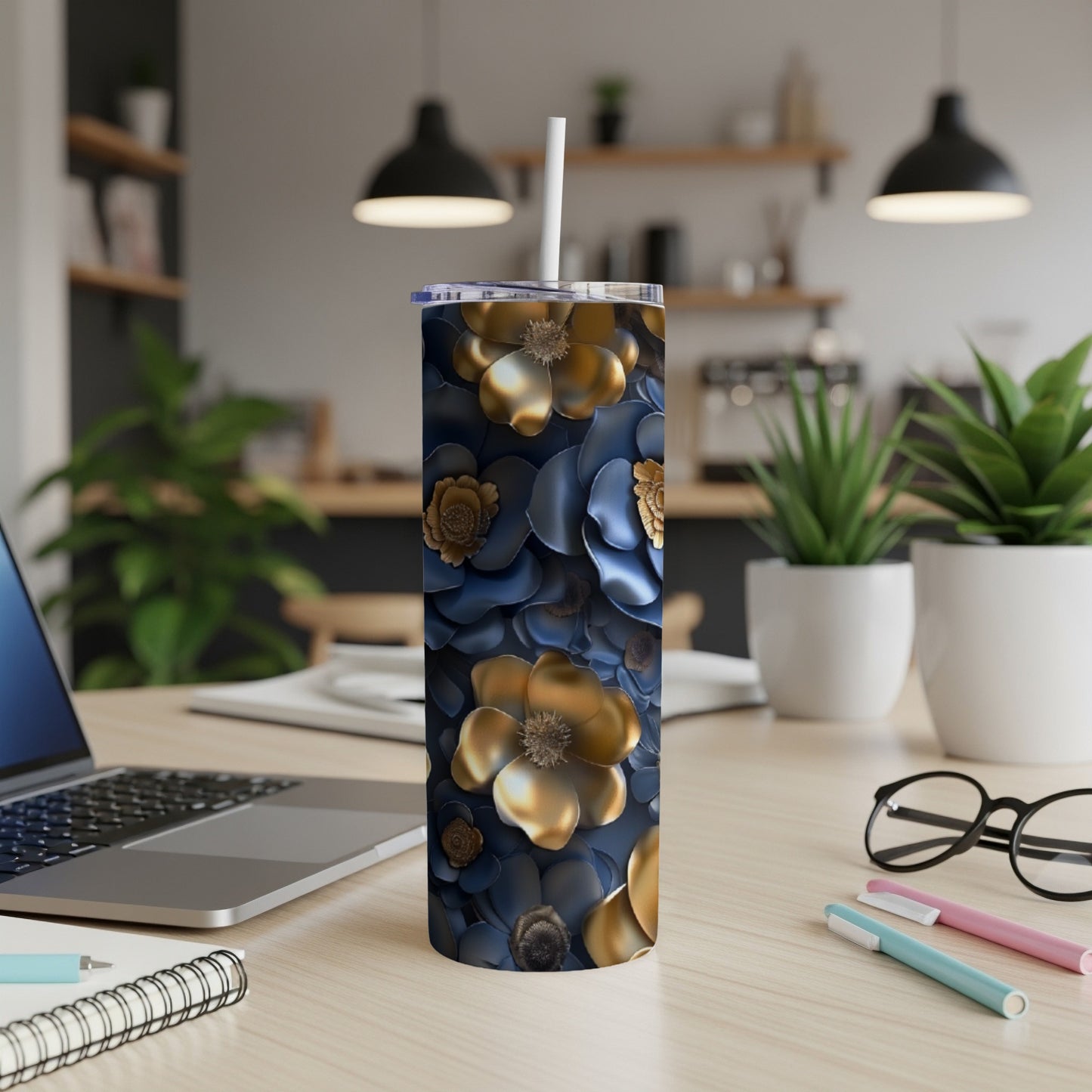 Blue and gold floral tumbler with straw on desk with laptop and pens.