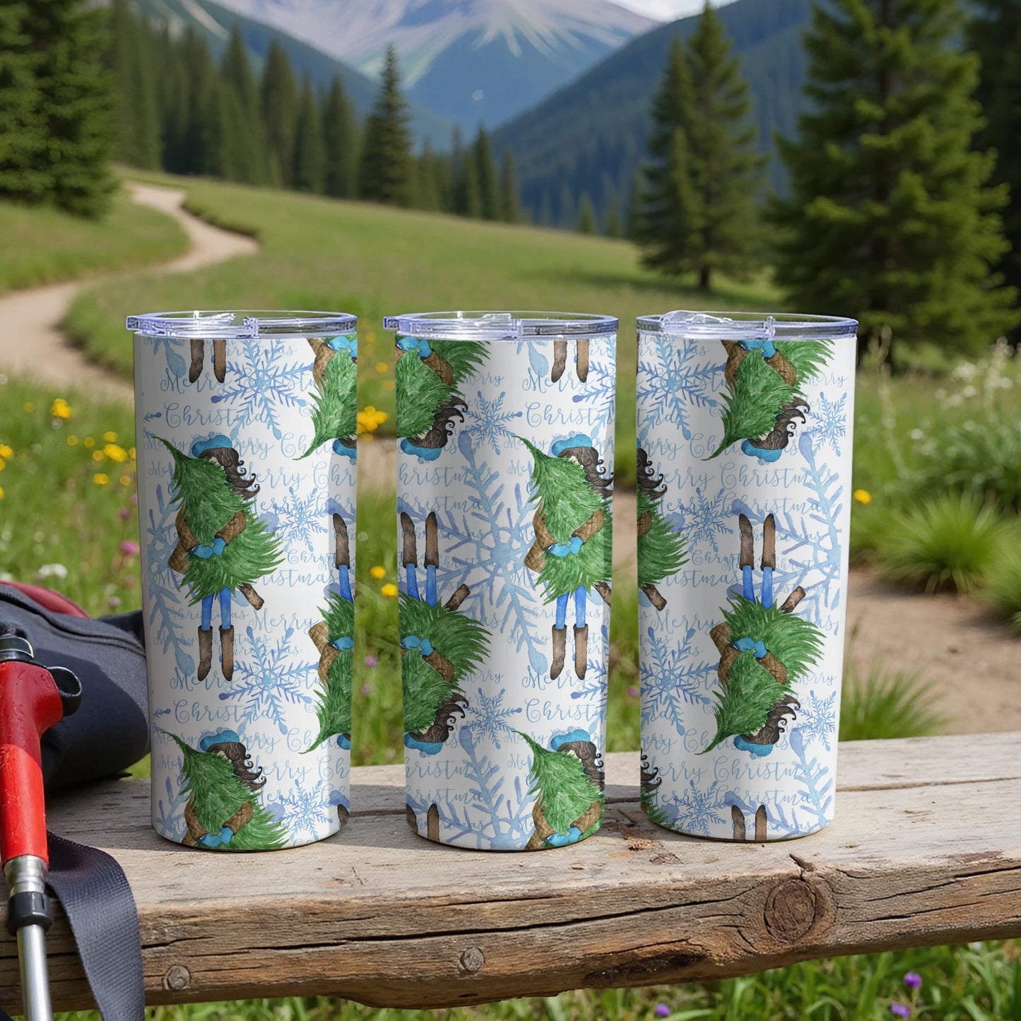 Three snow-covered pine trees in festive sweaters and hats on a skinny tumbler.