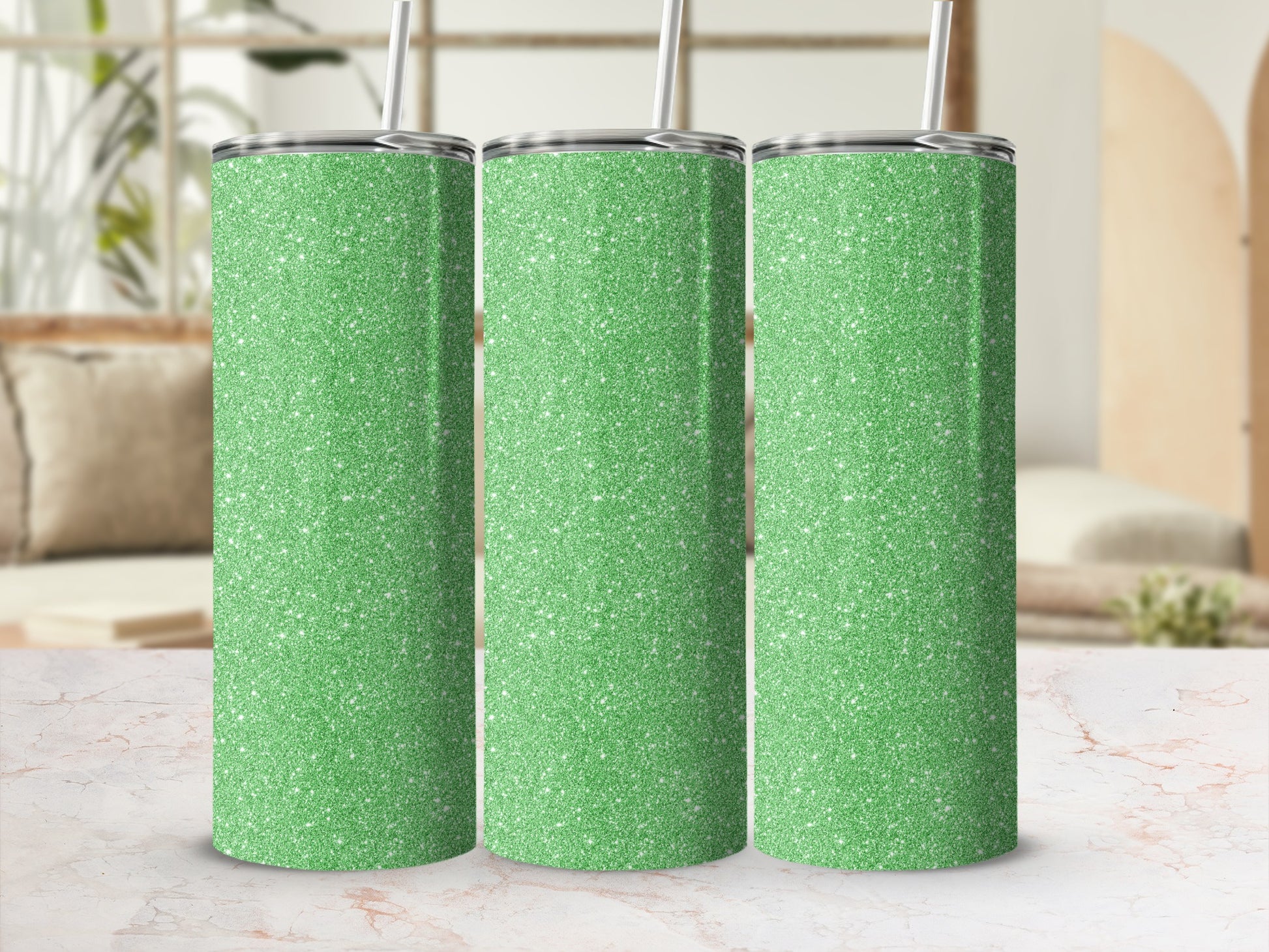 Three green glitter tumblers with straws on a marble surface.