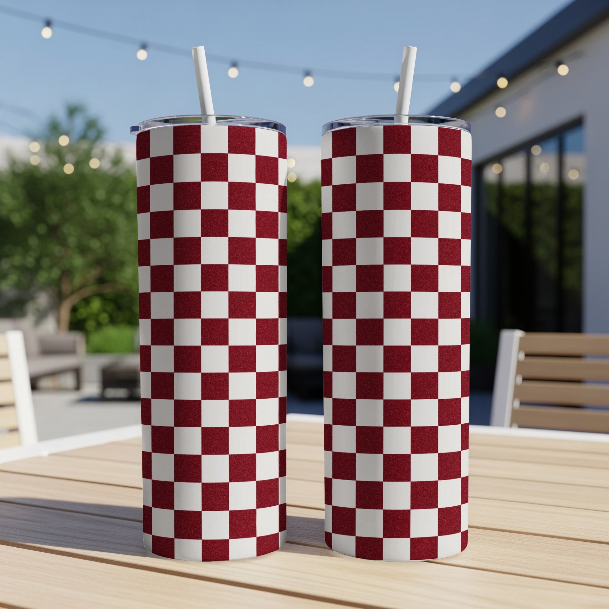 Two maroon and white checkered tumblers with straws on a wooden table.
