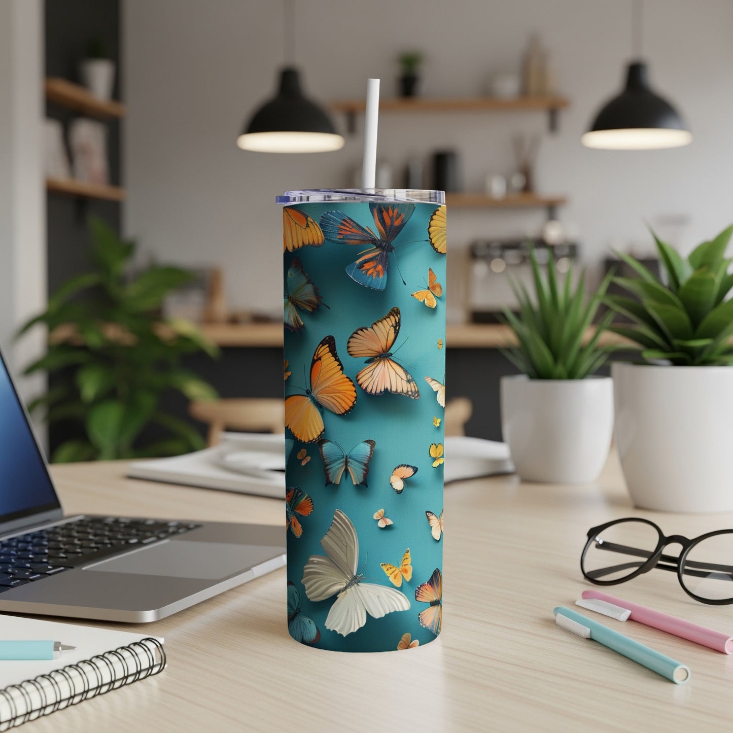 Teal tumbler with colorful butterflies, straw, and desk accessories.