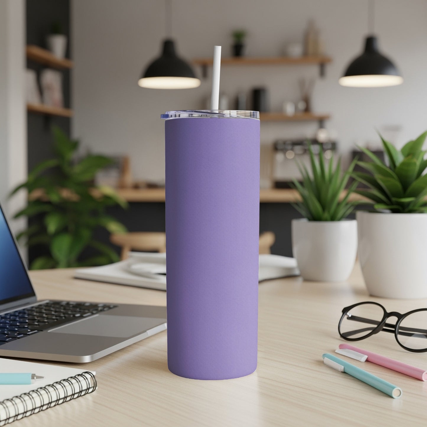 Purple tumbler with straw on a desk next to a laptop and pens.