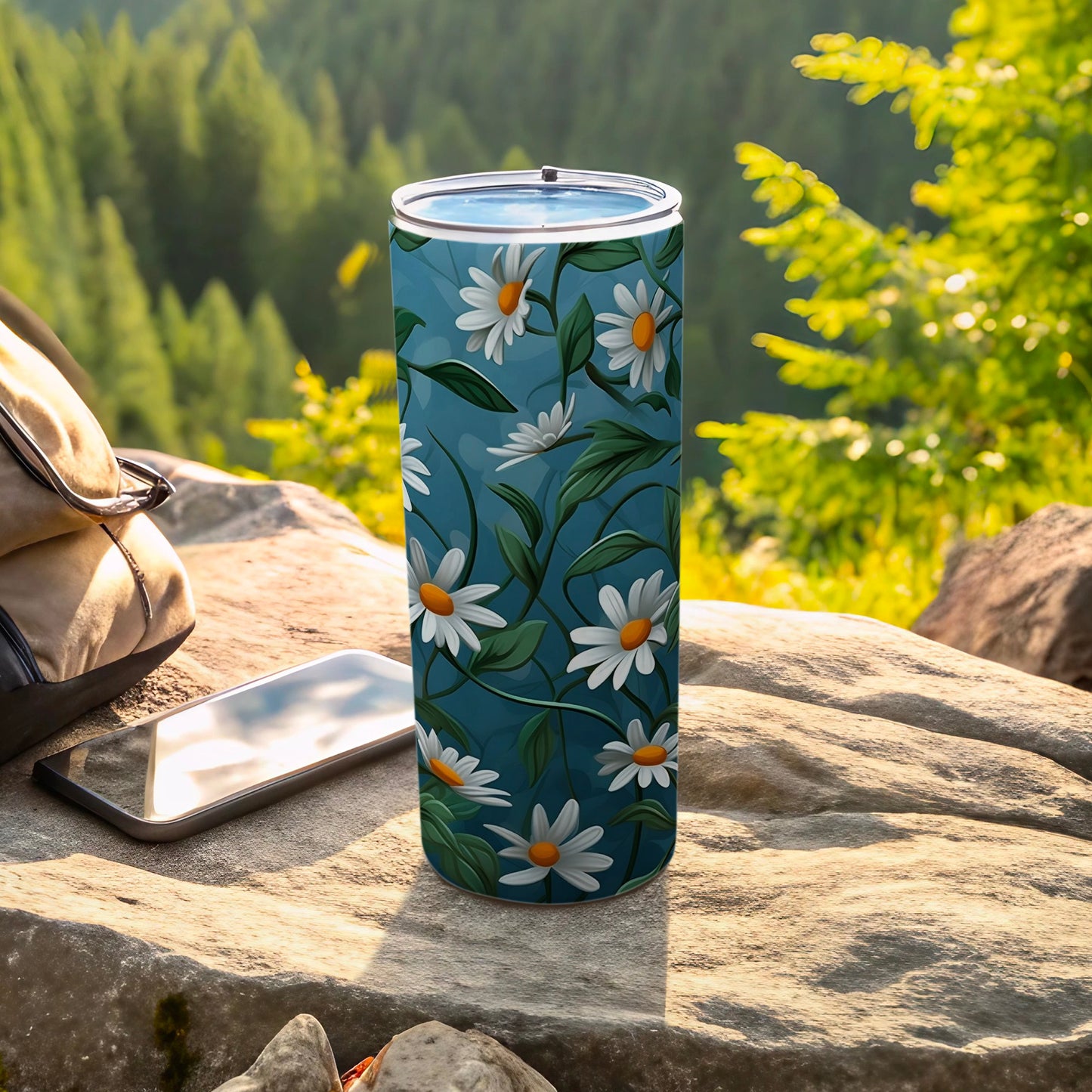 Blue tumbler with white daisies and green leaves, beside phone and backpack.