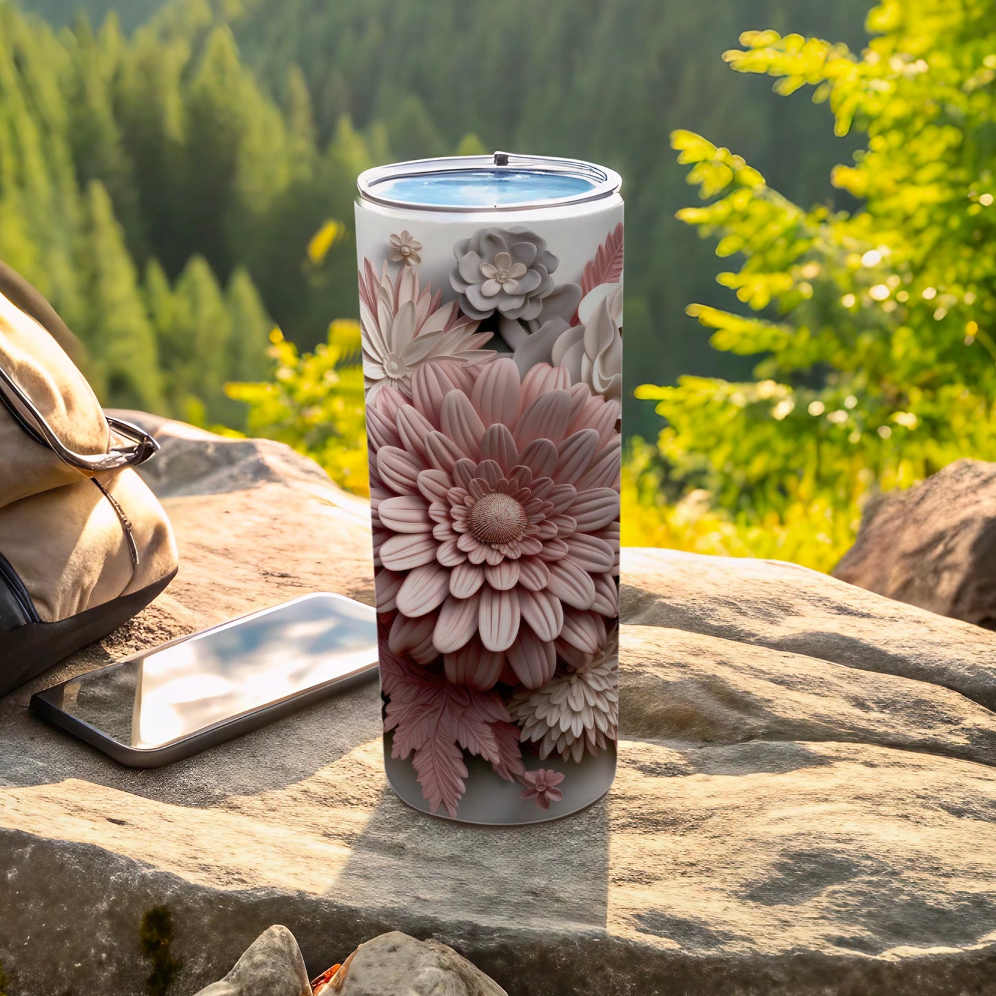 Pink floral tumbler on rock next to phone and backpack in outdoor setting.