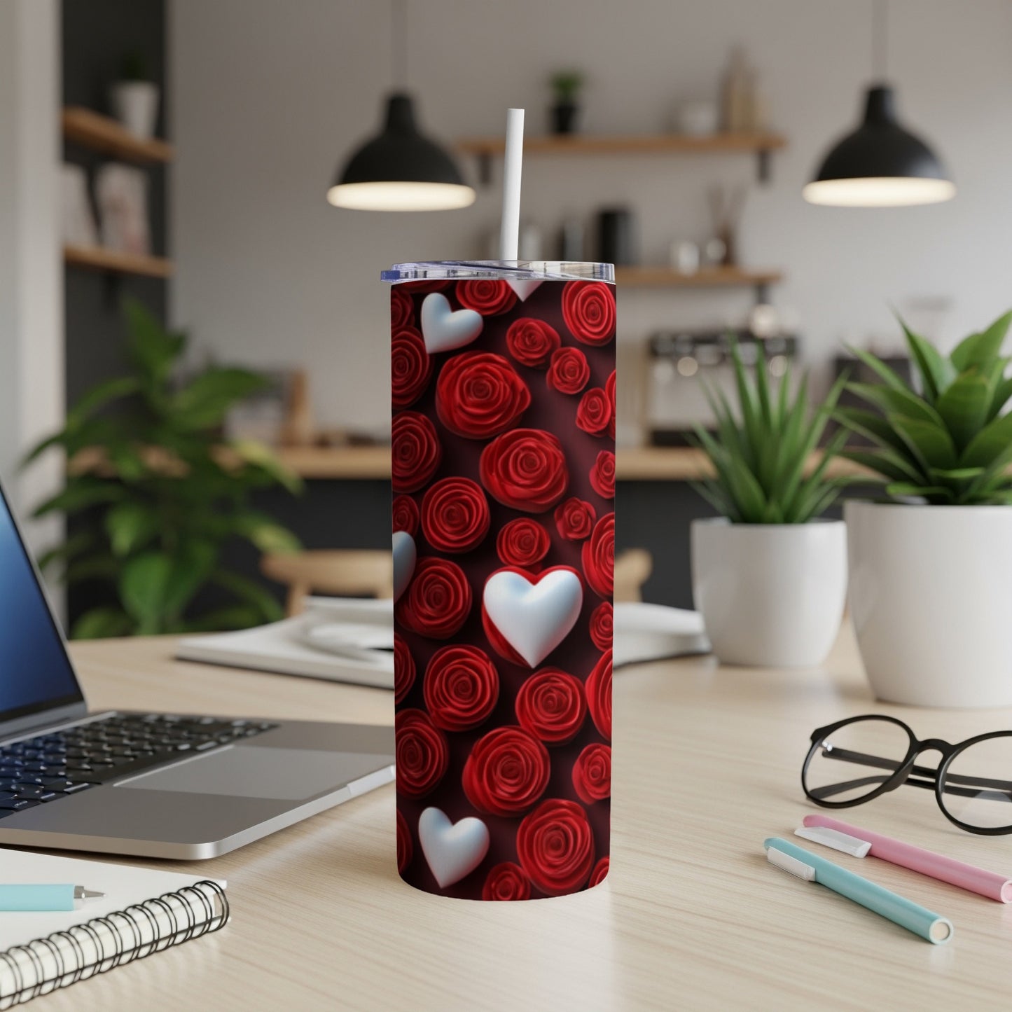 Red roses and white hearts pattern on a tumbler with a straw on a desk.