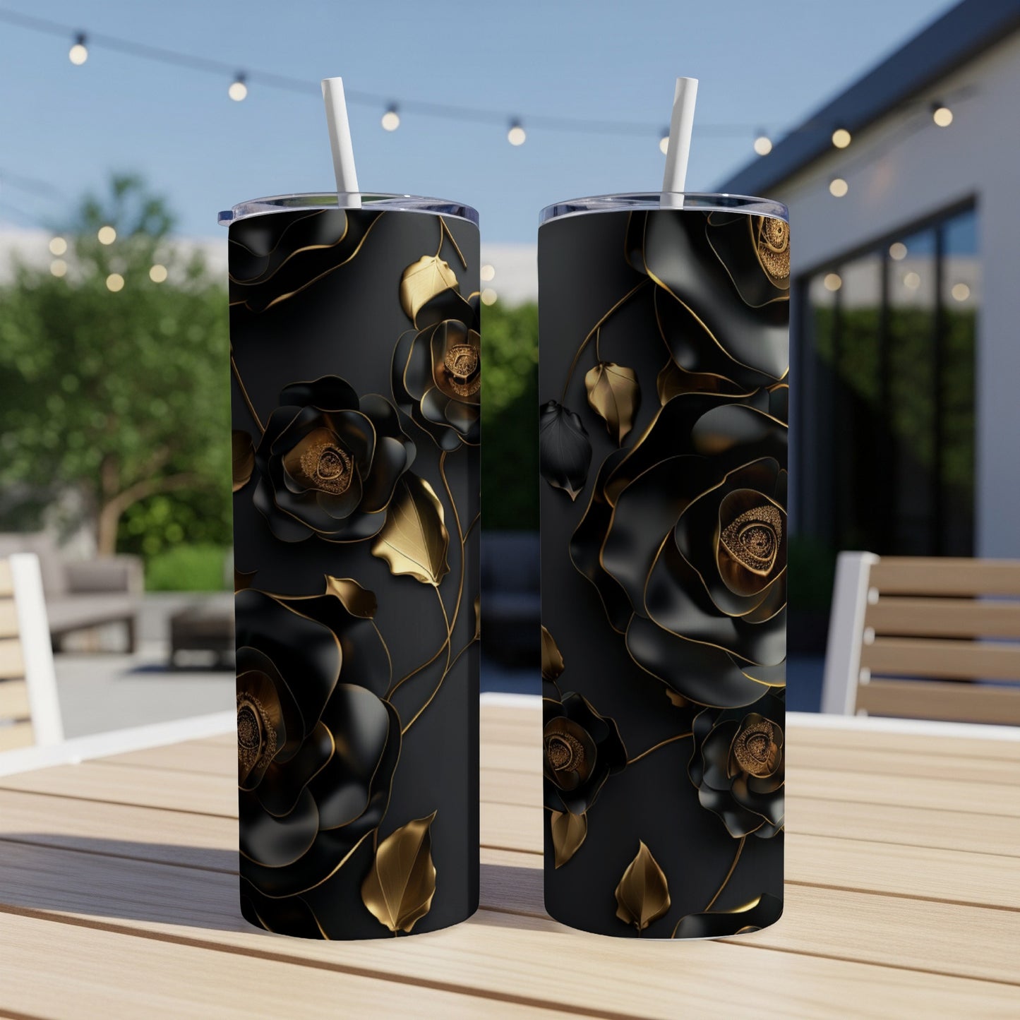 Two black tumblers with gold roses and leaves on a patio table.