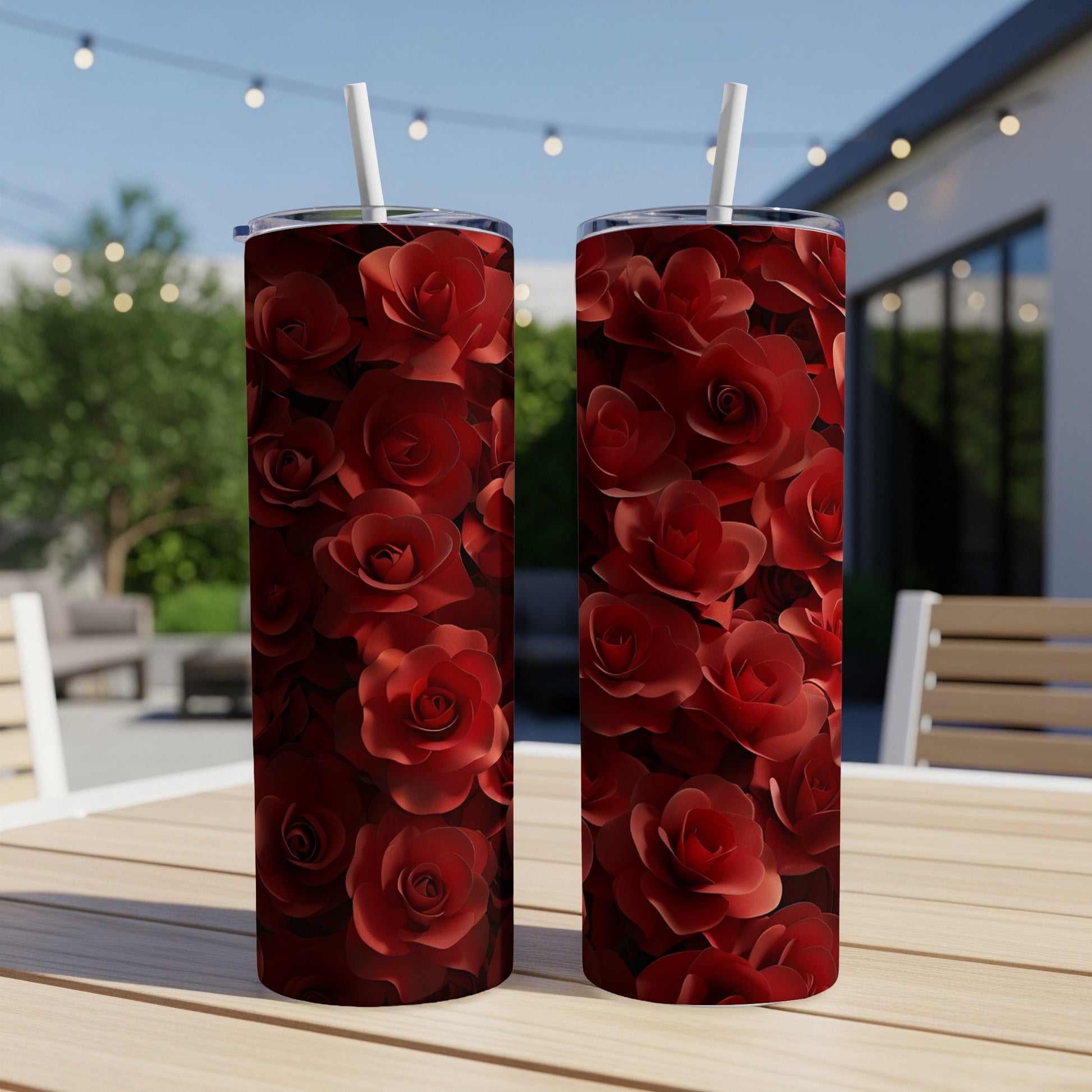 Two tumblers covered in red roses sit on a wooden table outdoors.