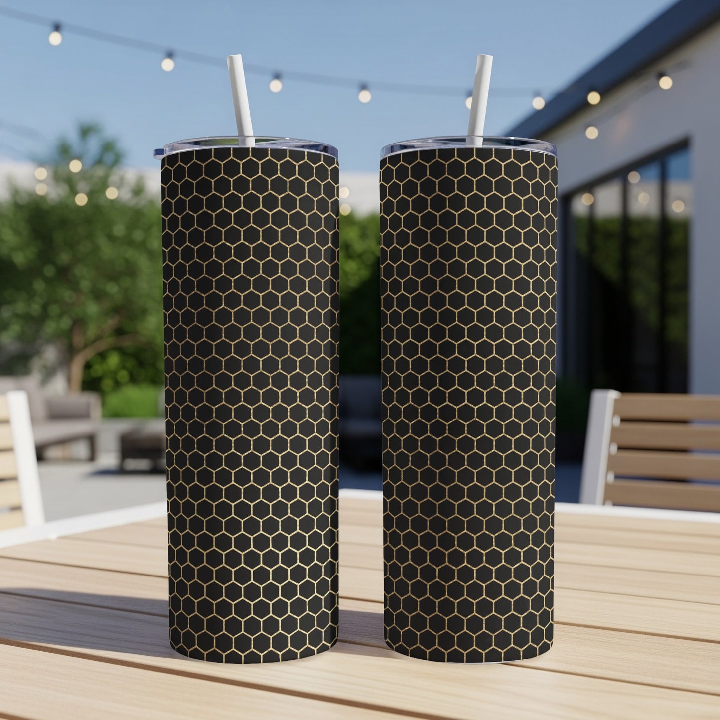 Two black tumblers with gold honeycomb pattern and white straws on a table.