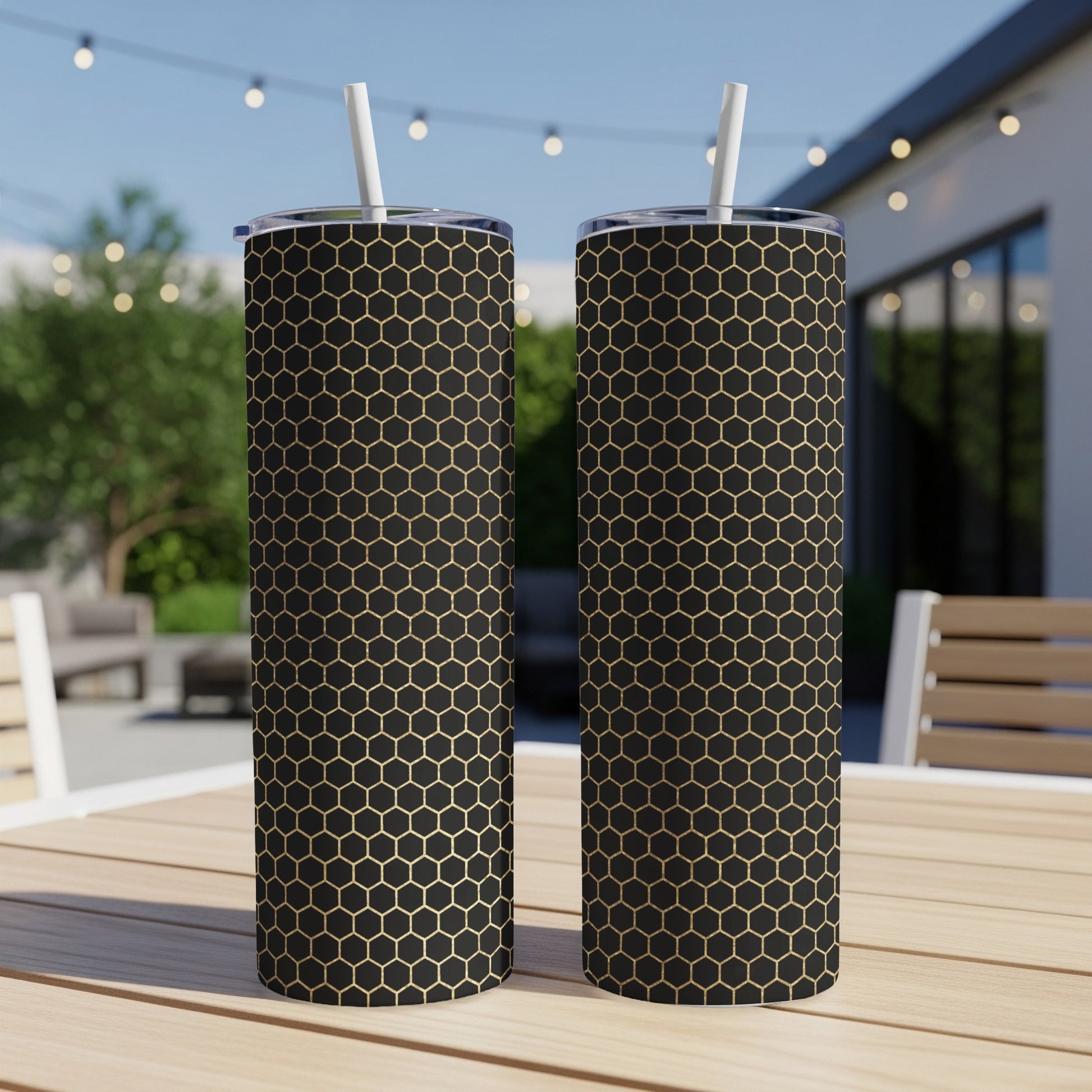Two black tumblers with gold honeycomb pattern and white straws on a table.